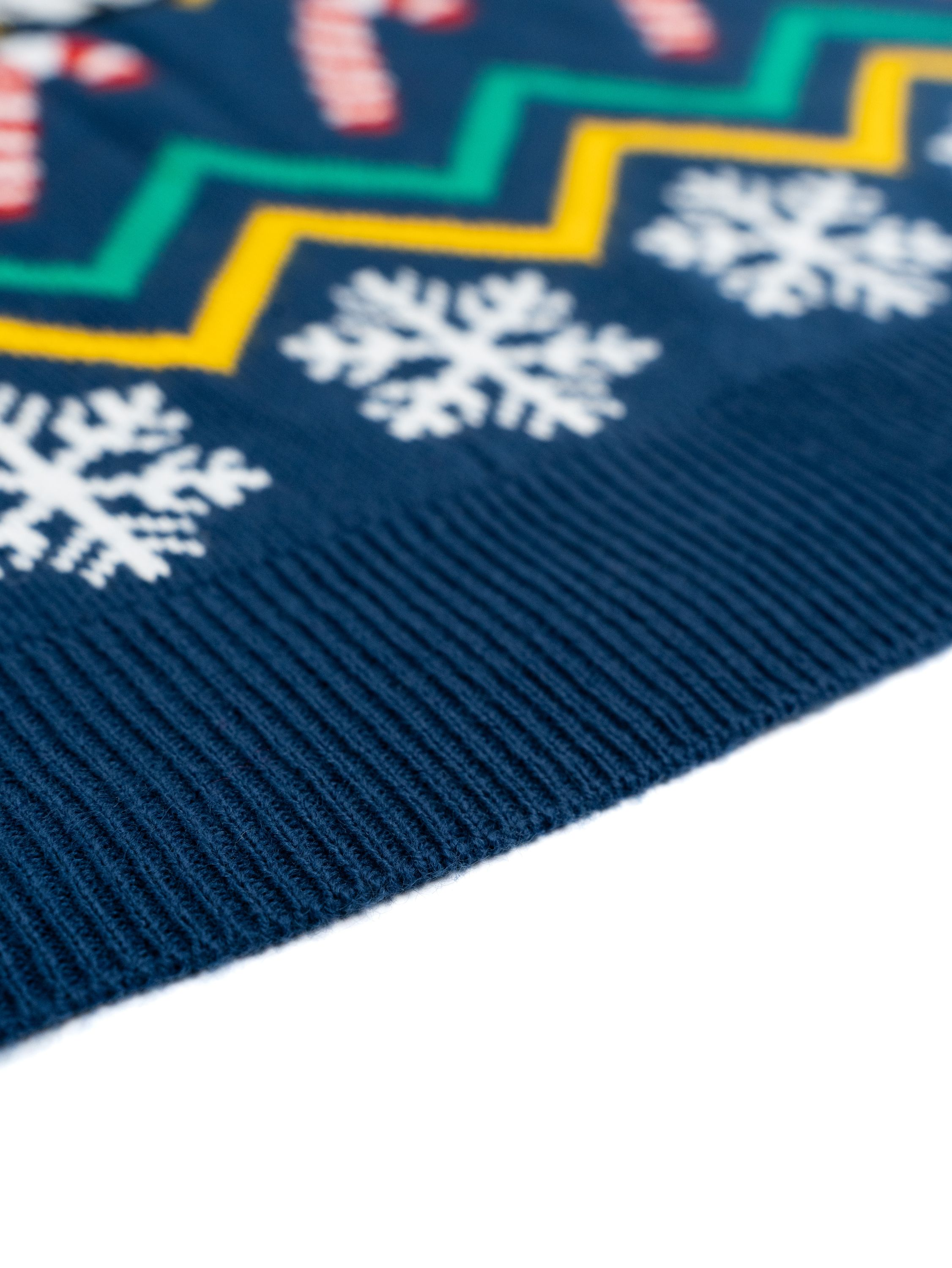 Nahaufnahme eines blauen Strickpullovers. Er hat weiße Schneeflocken und Zickzackmuster in Gelb und Grün.