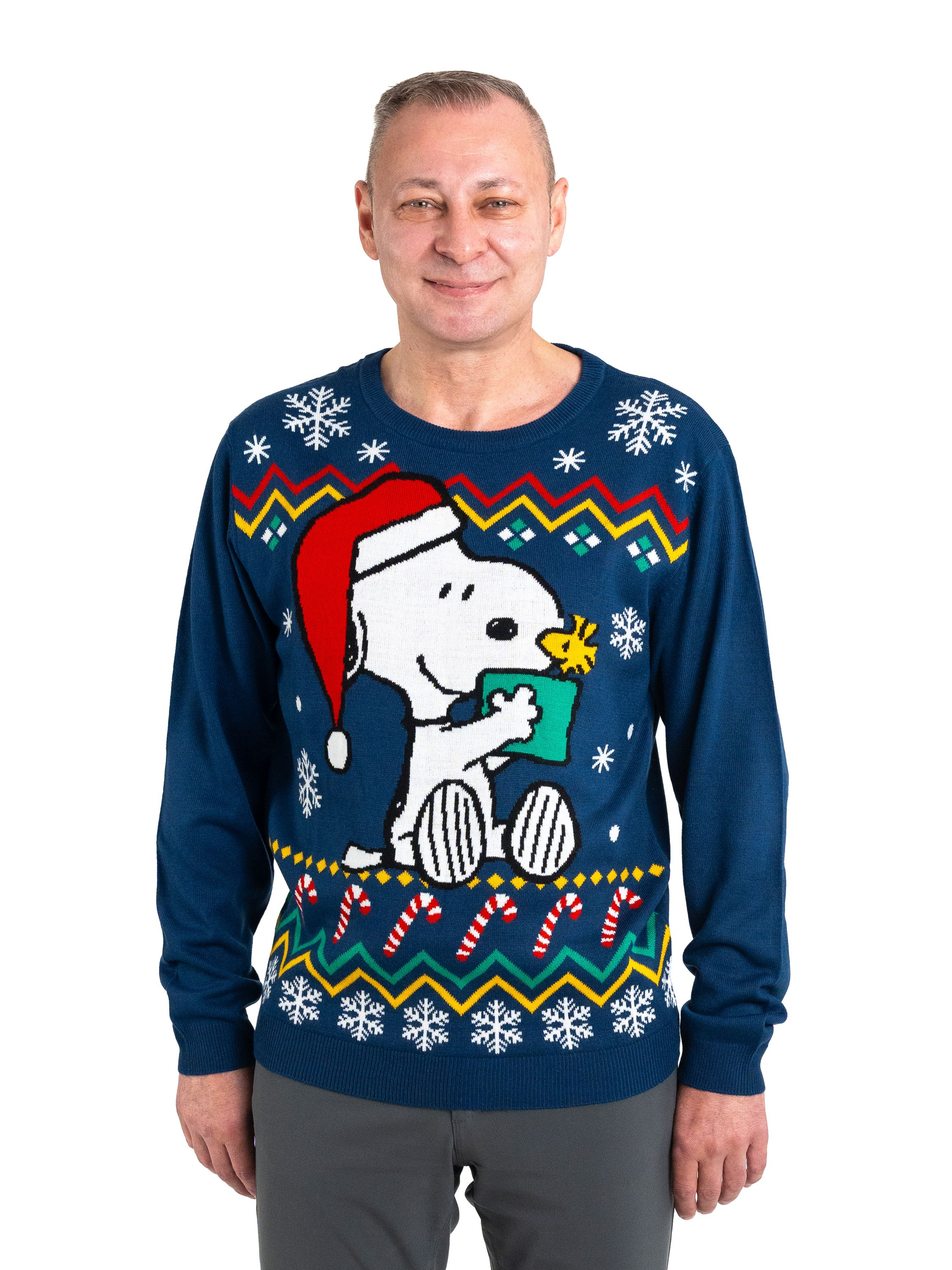 Mann trägt blauen Weihnachtspullover mit Snoopy, der ein Geschenk hält. Weißer Hintergrund.
