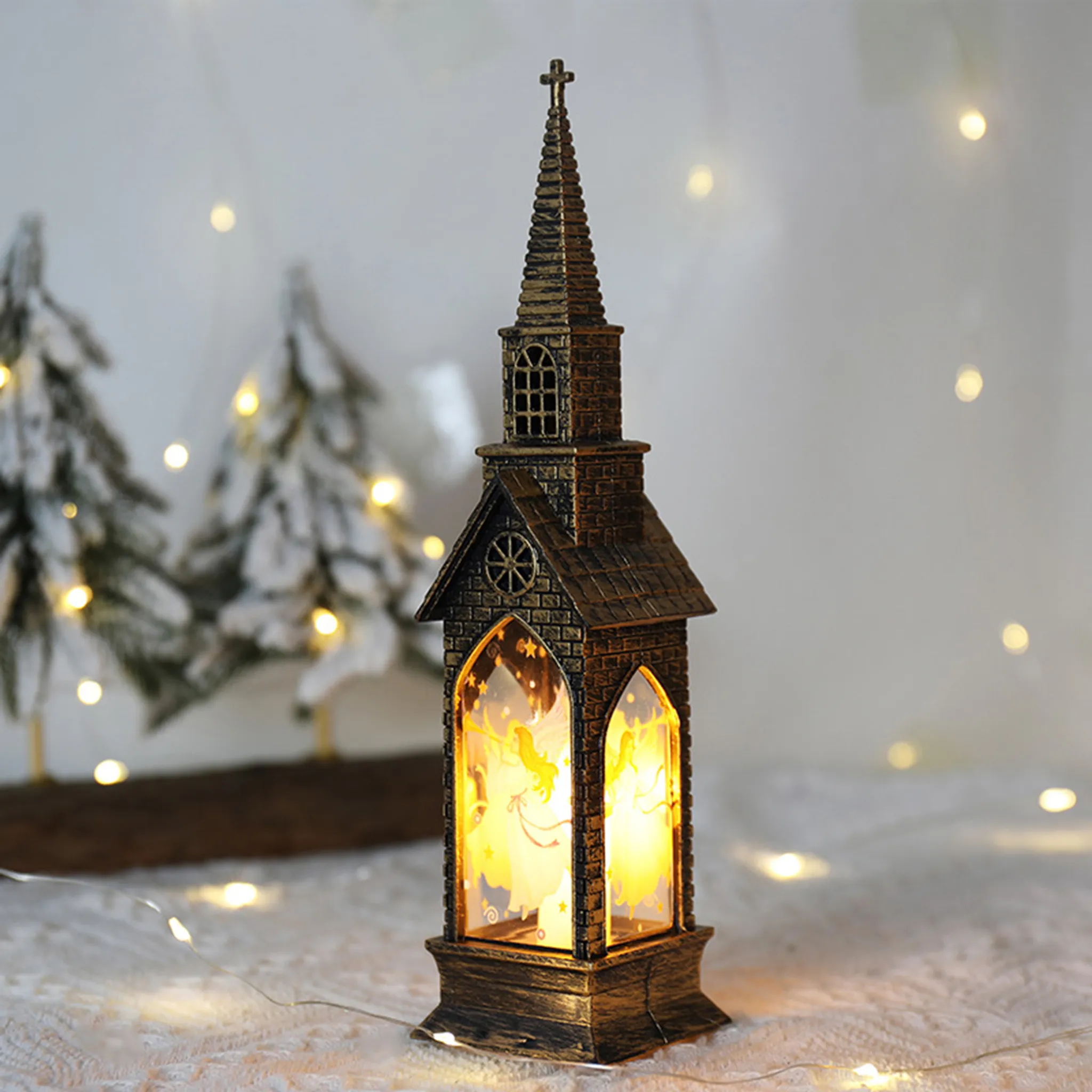 Eine kirchenförmige Laterne mit beleuchteten Engeln. Sie steht auf einer weißen Oberfläche mit Lichterketten und verschwommenen Weihnachtsbäumen.