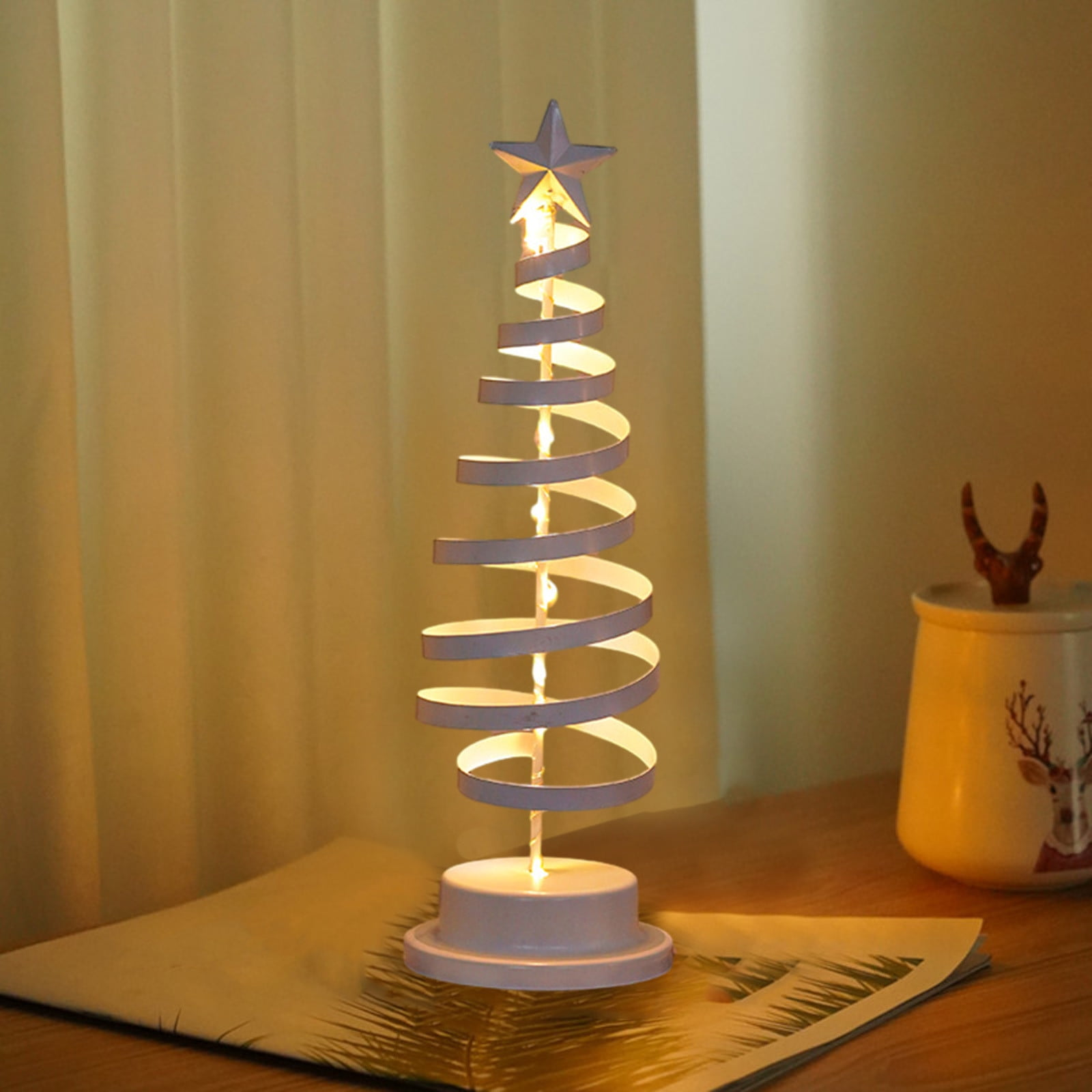 Eine dekorative Weihnachtsbaum-Lampe mit Stern, ein Glas mit Hirschmuster und eine Zeitung.