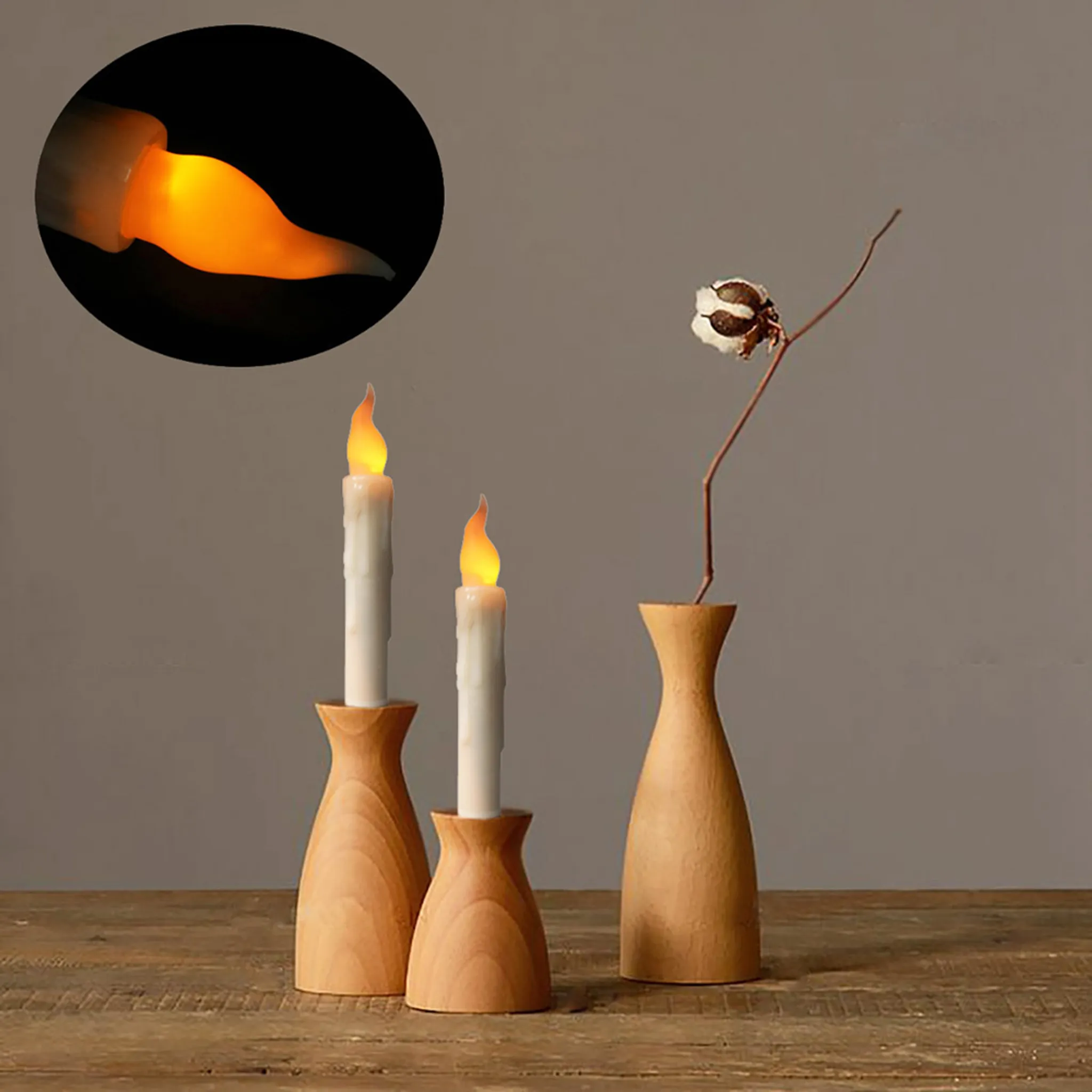 Das Bild zeigt drei hölzerne Kerzenhalter mit Kerzen und eine Vase mit Stiel und Blume vor grauem Hintergrund.