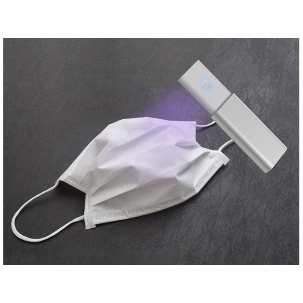 Una maschera bianca viene igienizzata con un dispositivo a luce UV su una superficie grigia. La maschera è a sinistra, il dispositivo a destra.