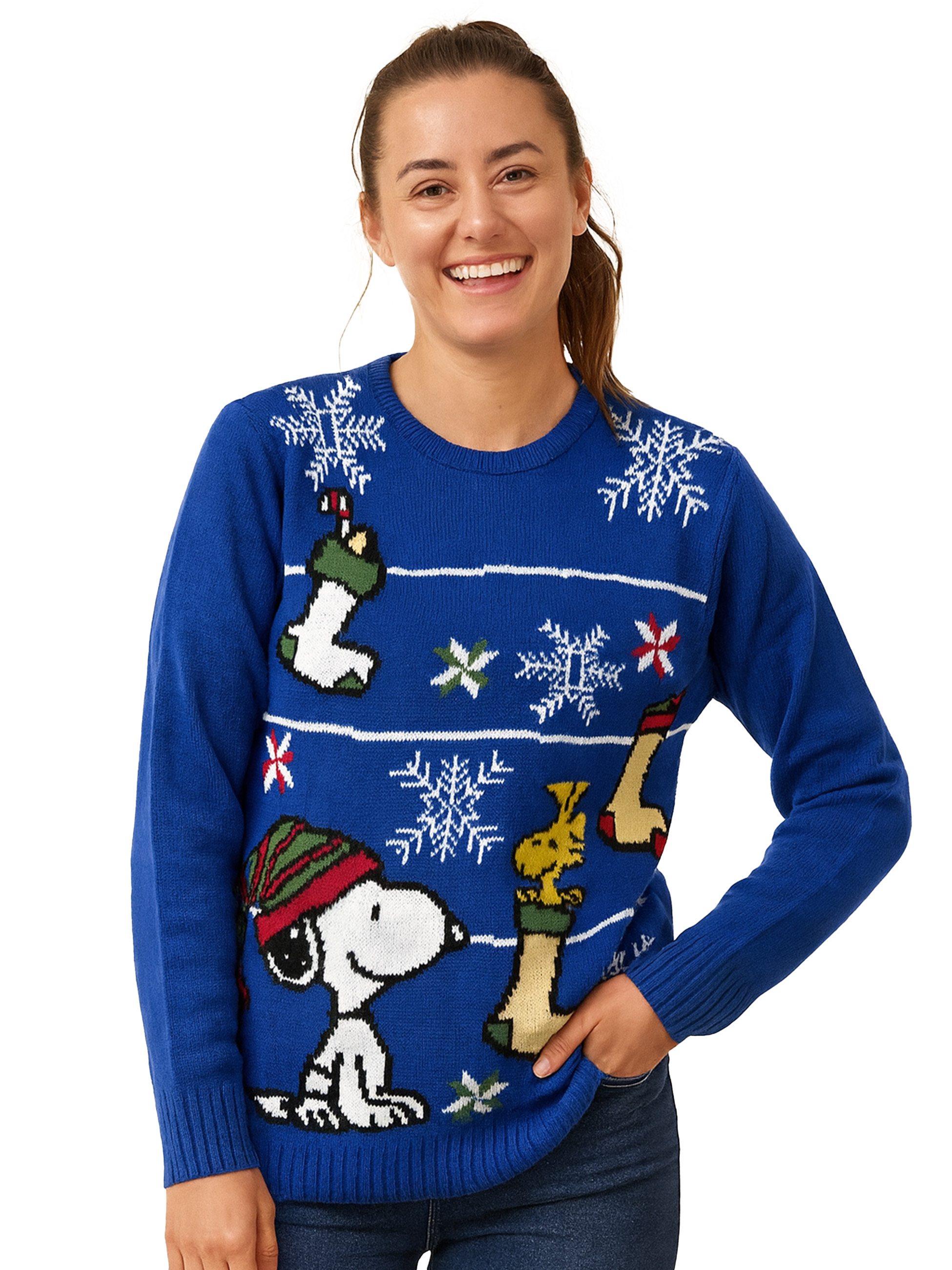 Frau in blauem Weihnachtspullover mit Snoopy und Schneeflocken. Sie lächelt, Hand in der Tasche.