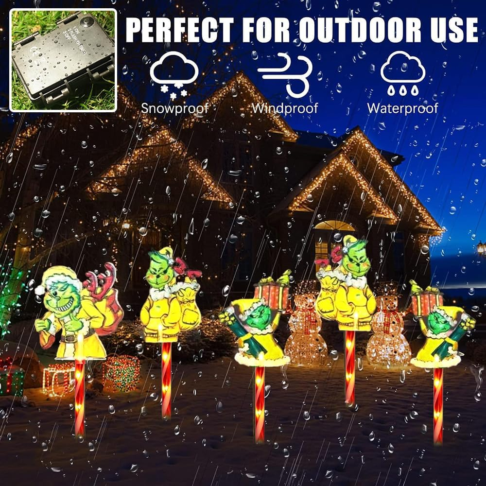 Grinch-Gartendekorationen. Die Grinch-Figuren stehen auf Zuckerstangenpfählen mit einem Haus und Regen im Hintergrund.
