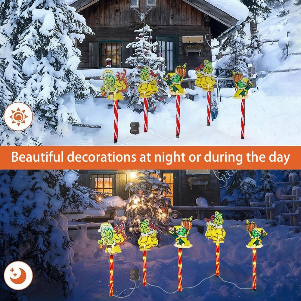 Weihnachtsdekorationen: Grinch-Figuren auf Zuckerstangen-Pfählen im Schnee. Ein Haus und Bäume sind im Hintergrund. Überall liegt Schnee.