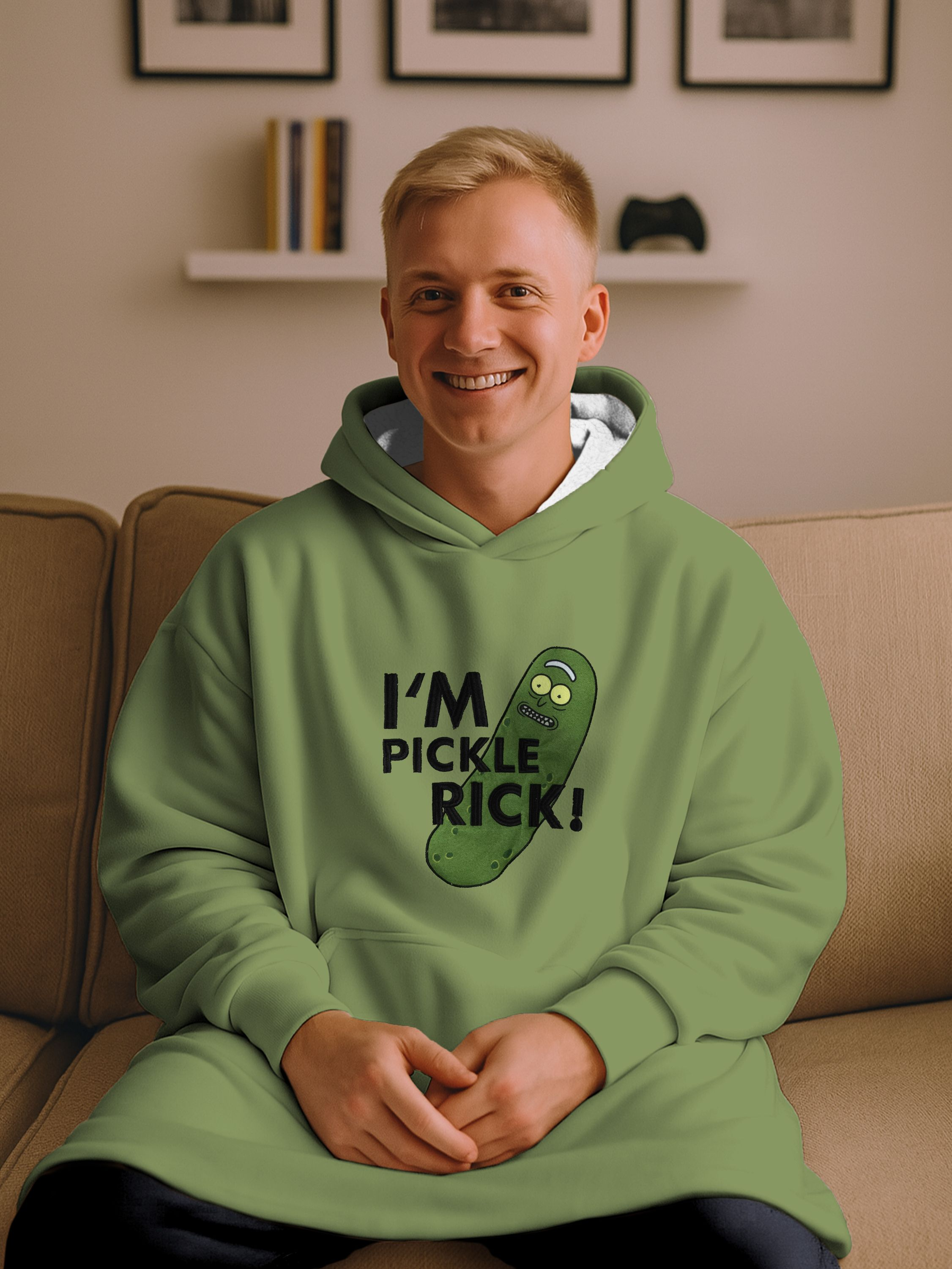 Mann trägt grünen Hoodie mit 'Ich bin Pickle Rick!'-Aufdruck, sitzt lächelnd auf Couch.