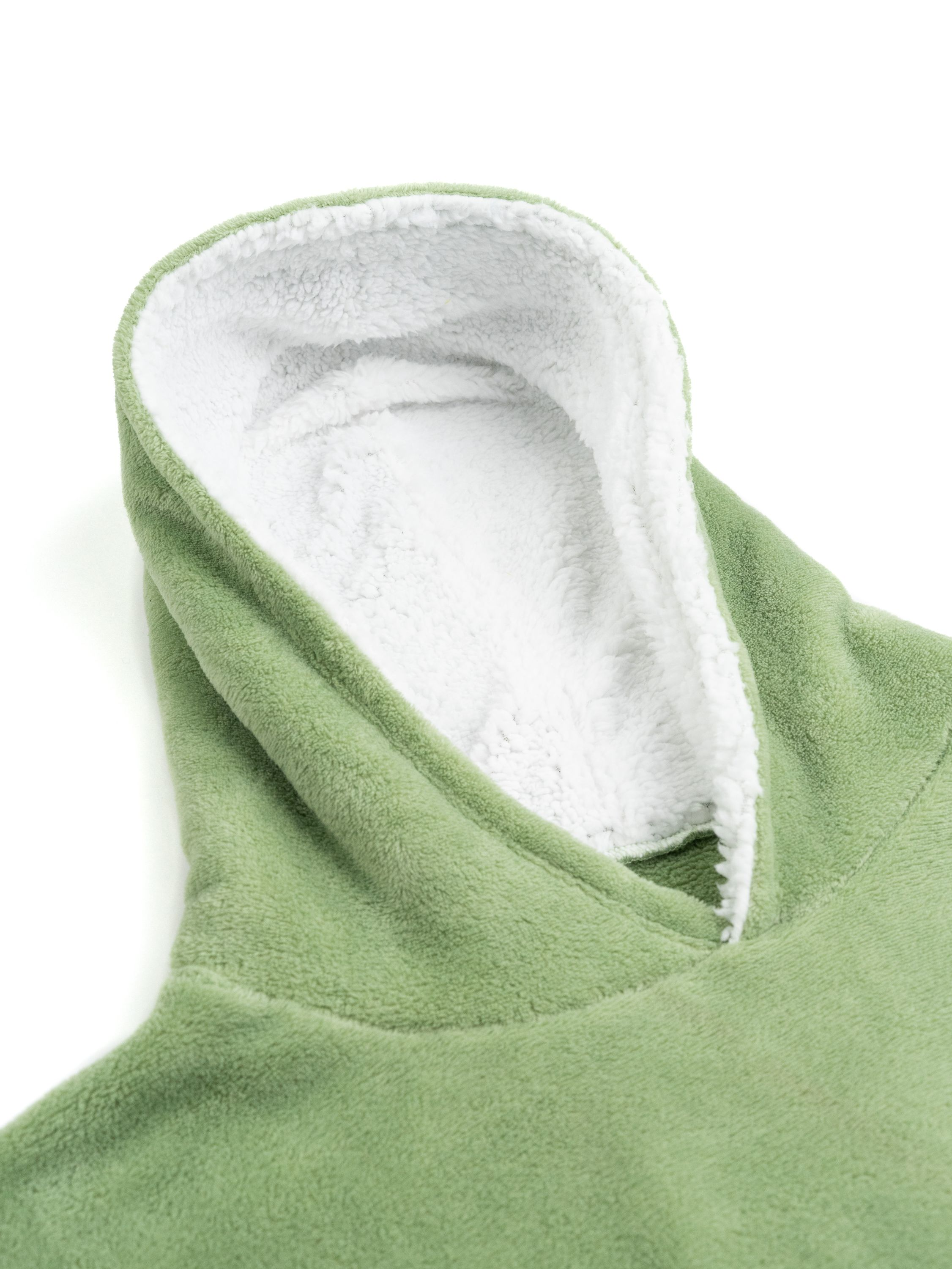 Eine grüne Kapuzendecke mit weißem, flauschigem Innenfutter liegt auf einer weißen Oberfläche. Die Kapuze ist im Fokus.