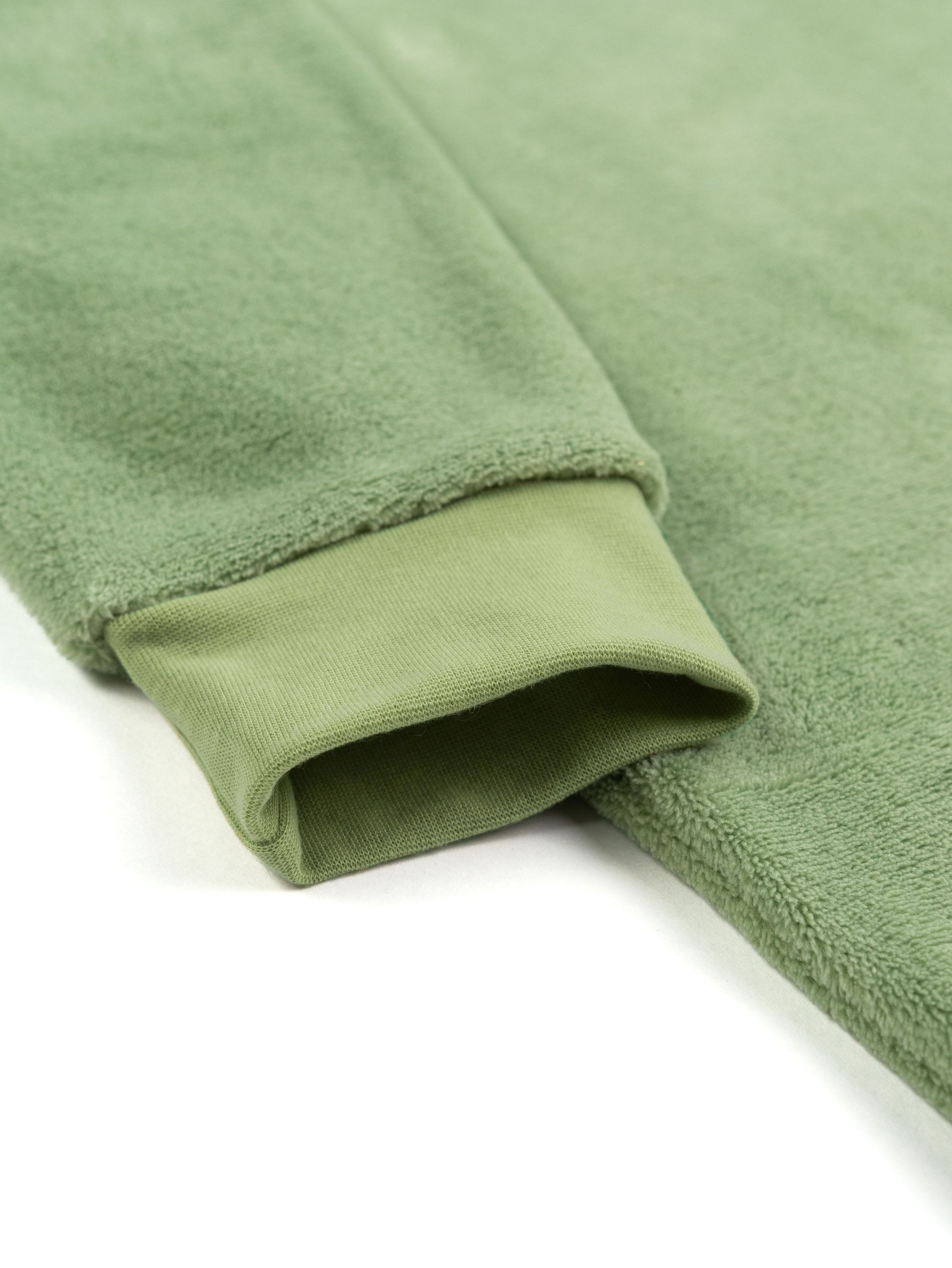 Nahaufnahme eines grünen Sweatshirtärmels mit geripptem Bündchen. Der Hintergrund ist weiß.