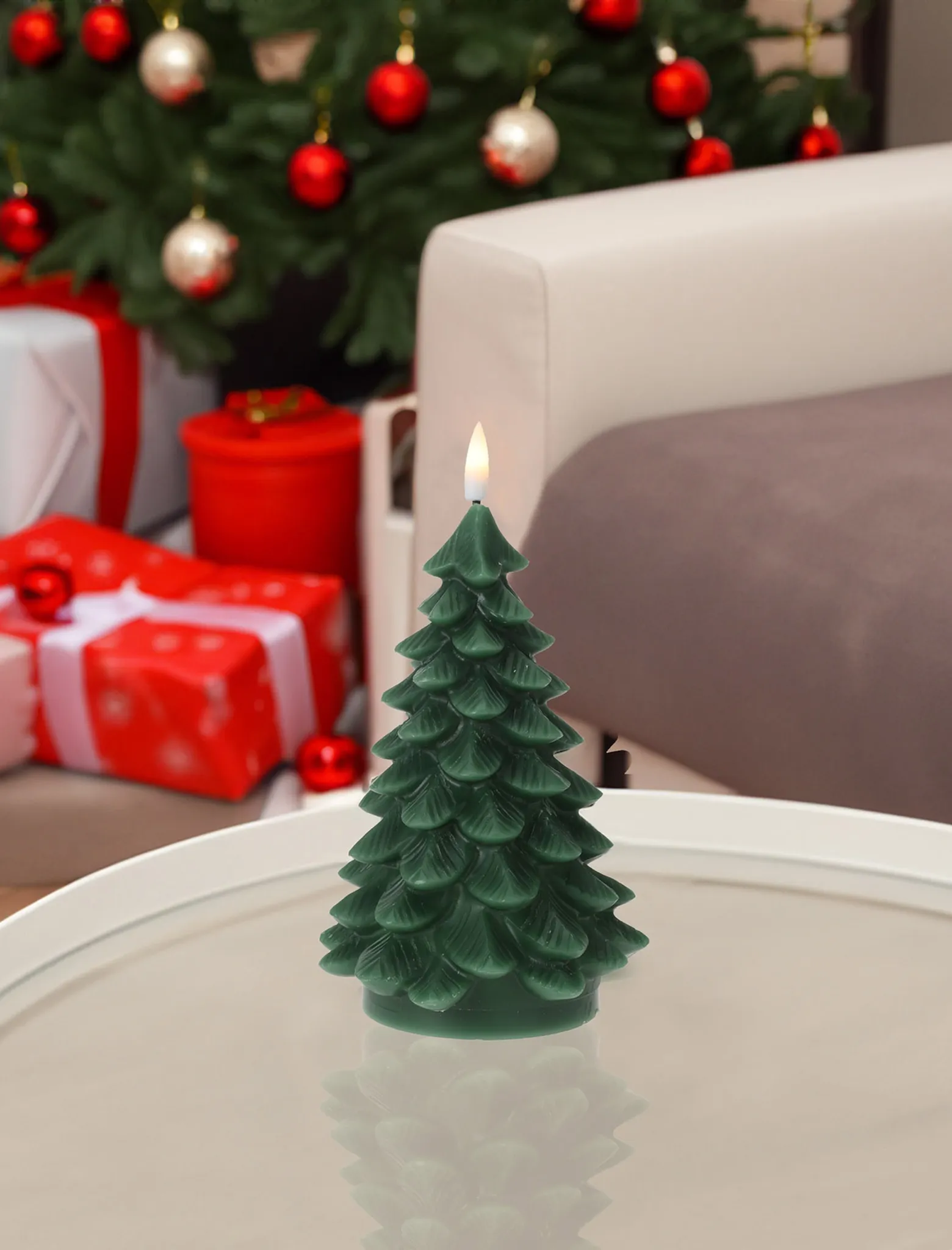 Eine grüne Weihnachtsbaumkerze mit Flamme. Geschenke und ein geschmückter Weihnachtsbaum im verschwommenen Hintergrund.