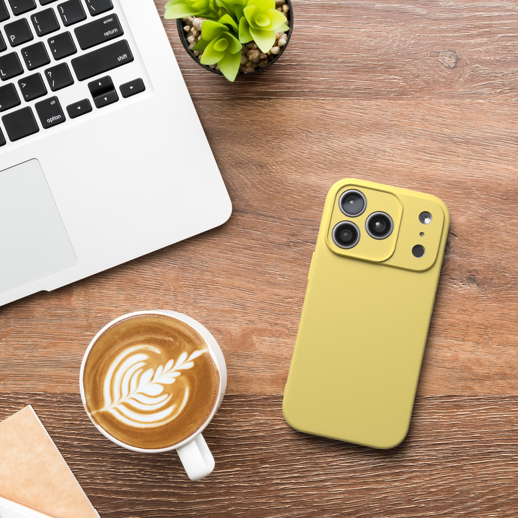 Ein Laptop, ein gelbes Telefon, eine Kaffeetasse mit Latte Art und eine kleine Pflanze auf einem Holztisch.