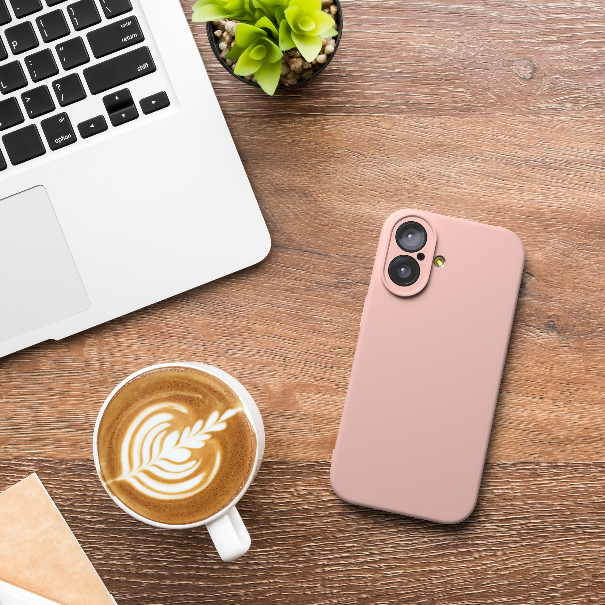 Ein Laptop, eine Kaffeetasse, ein rosa Telefon und eine Pflanze auf einem Holztisch. Kaffee hat ein Blattdesign.