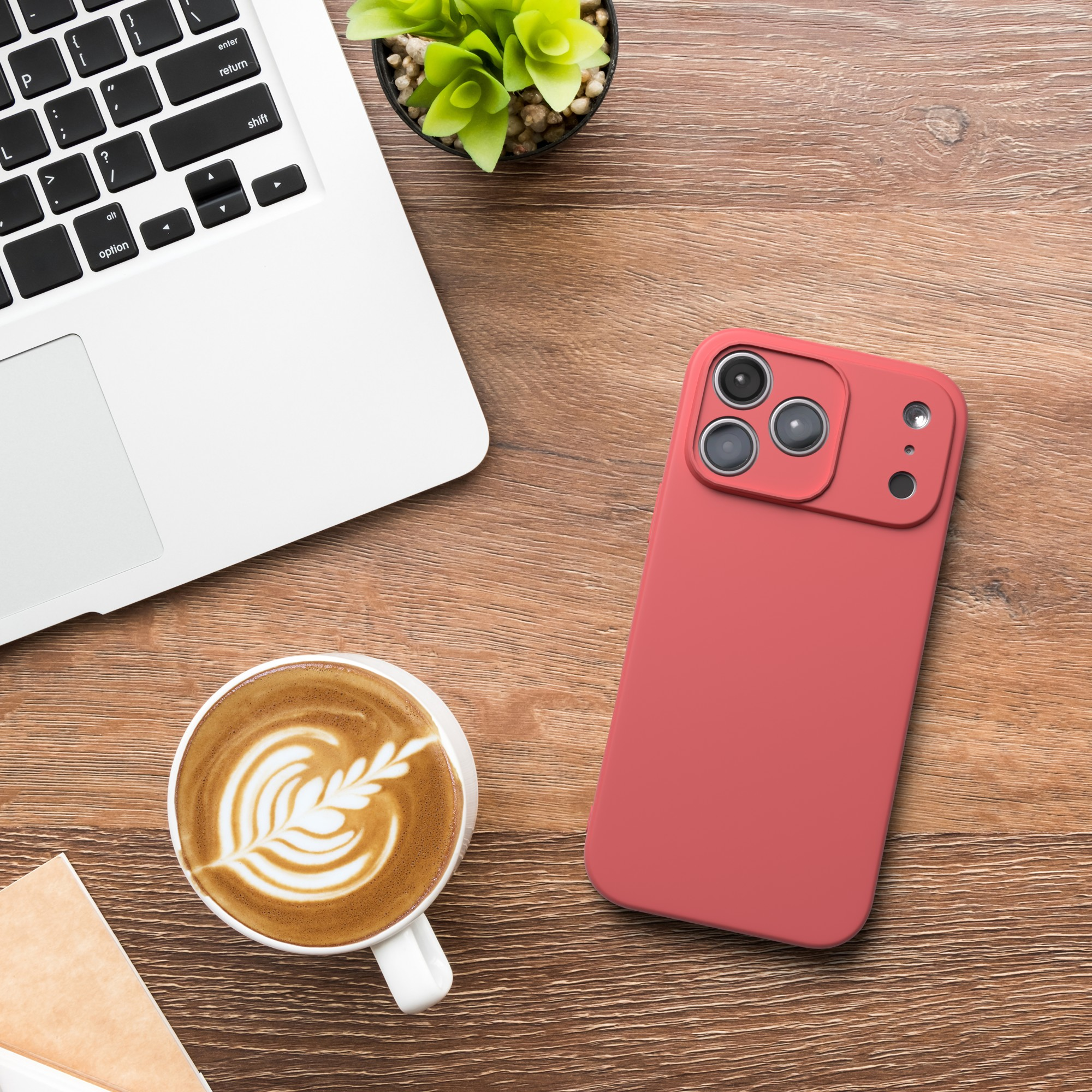 Ein Schreibtisch mit Laptop, Kaffee, Telefon und Pflanze. Das Telefon ist rot. Der Kaffee hat Latte Art.