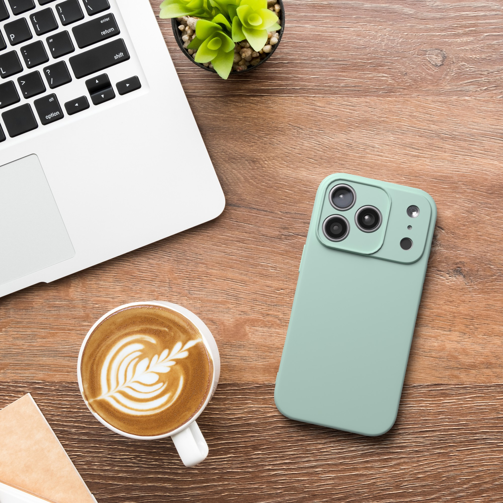 Ein Laptop, ein Telefon und eine Kaffeetasse auf einem Holztisch. Das Telefon ist grün. Kaffee hat Latte Art.