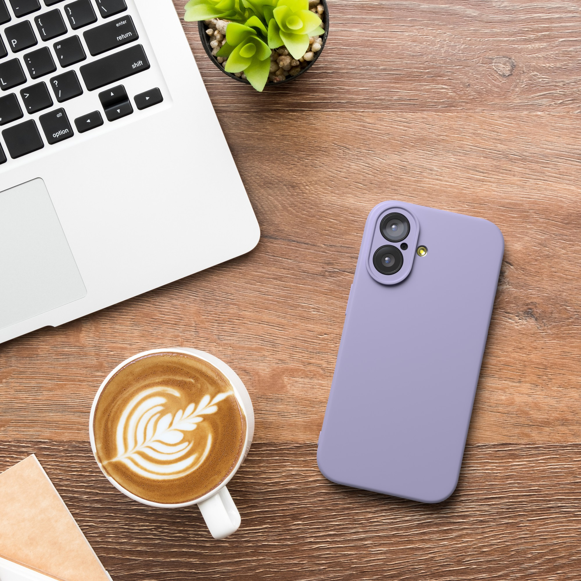 Ein Laptop, eine Kaffeetasse mit Latte Art, ein lila Telefon und eine kleine Pflanze auf einem Holztisch.