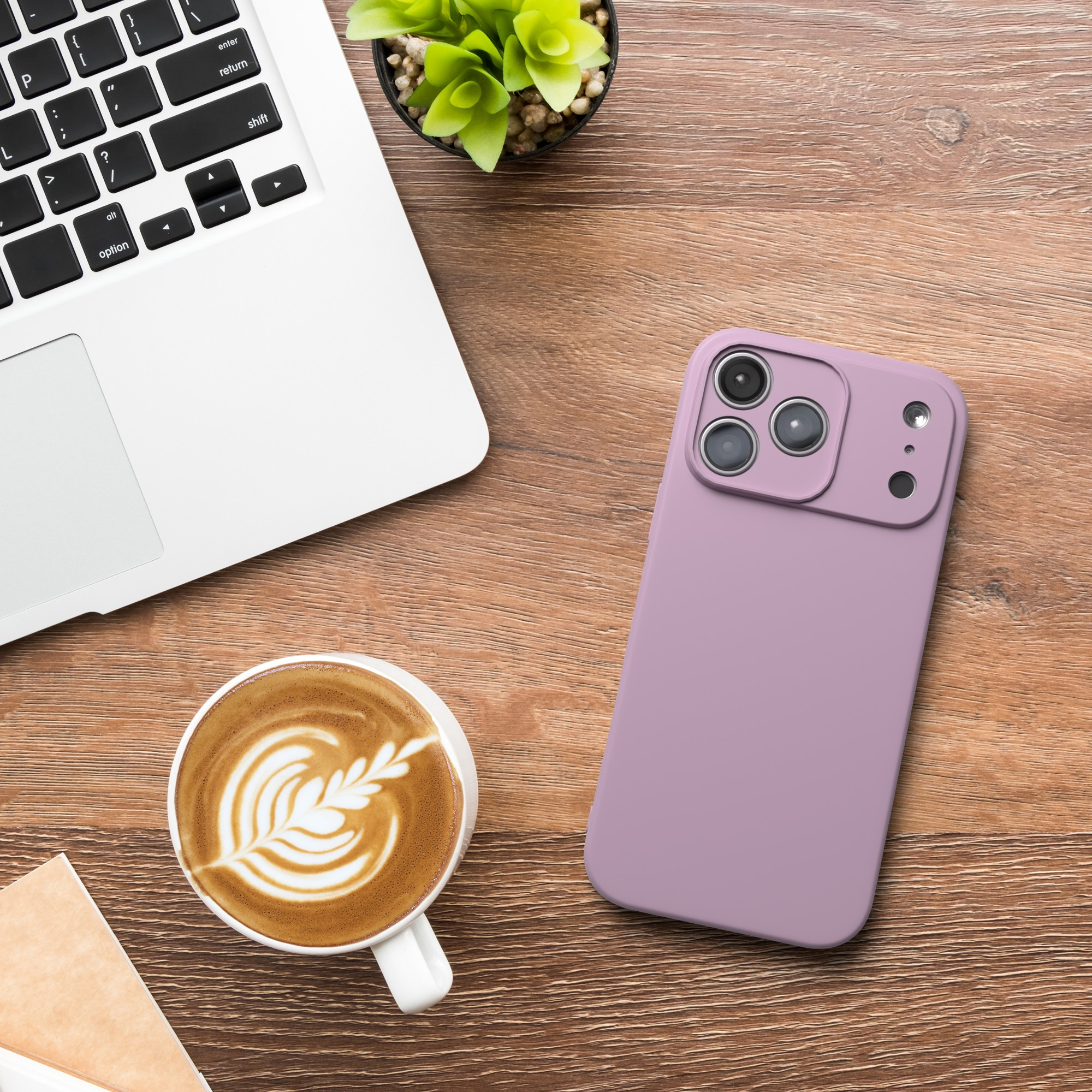 Ein Laptop, Kaffee mit Latte Art, ein Telefon mit lila Hülle und eine Pflanze liegen auf einem Holztisch.