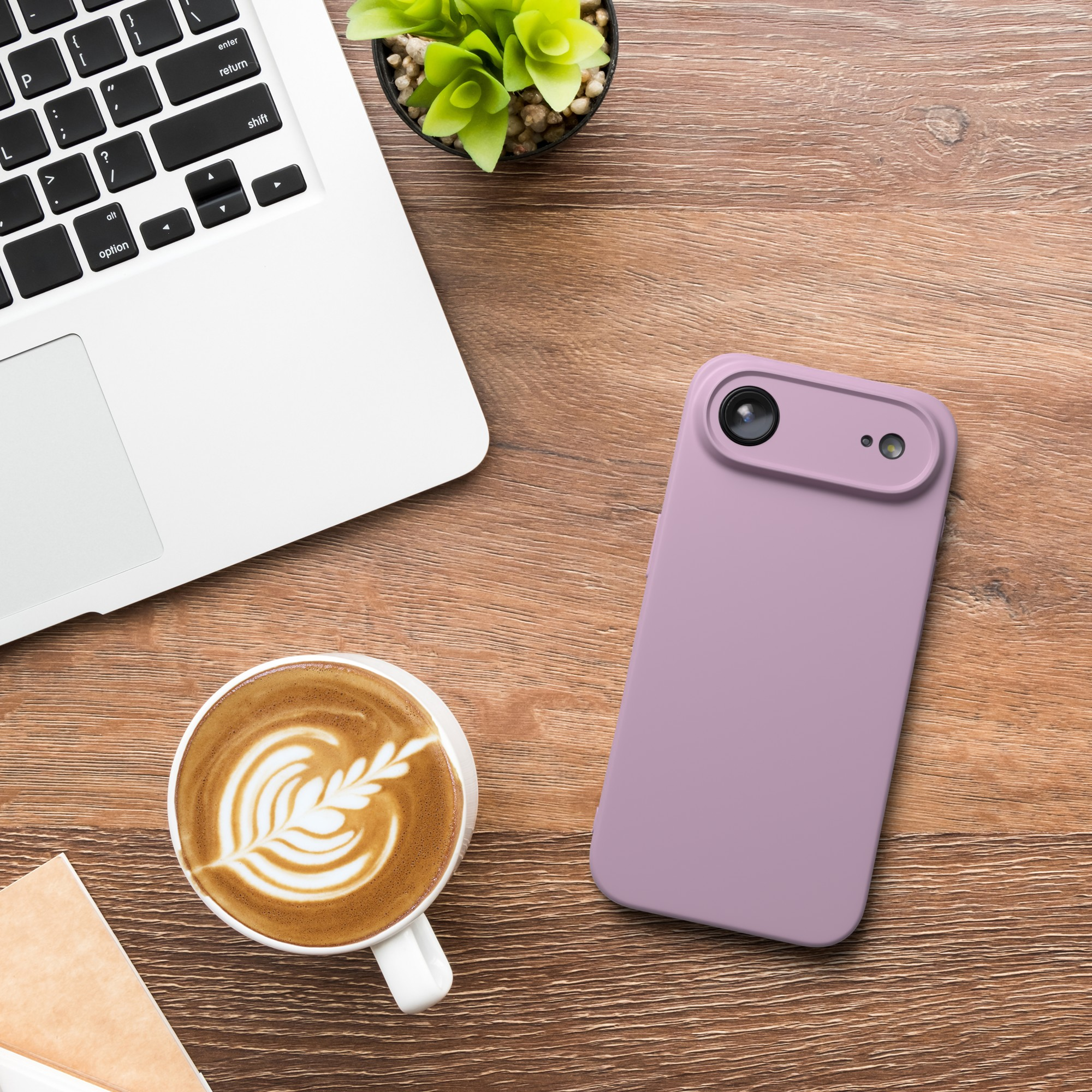 Ein Laptop, Kaffee mit Latte Art, ein Telefon und eine Pflanze auf einem Holztisch.