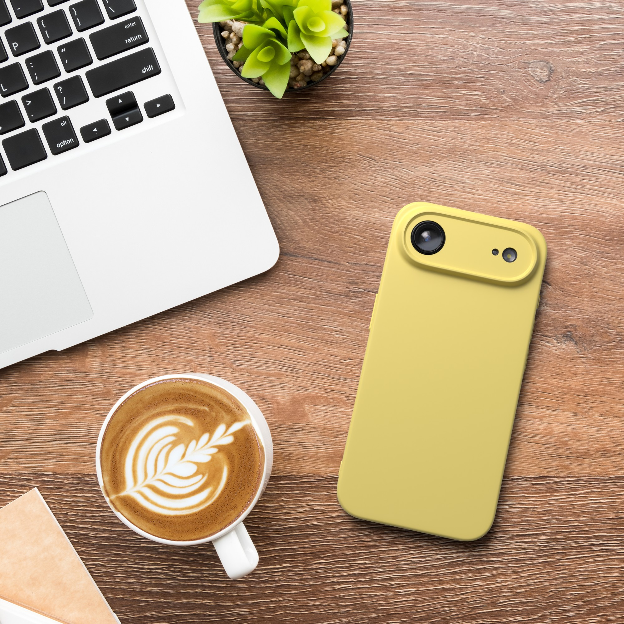 Ein Laptop, Kaffee mit Latte Art, ein gelbes Telefon und eine kleine Pflanze stehen auf einem Holzschreibtisch.