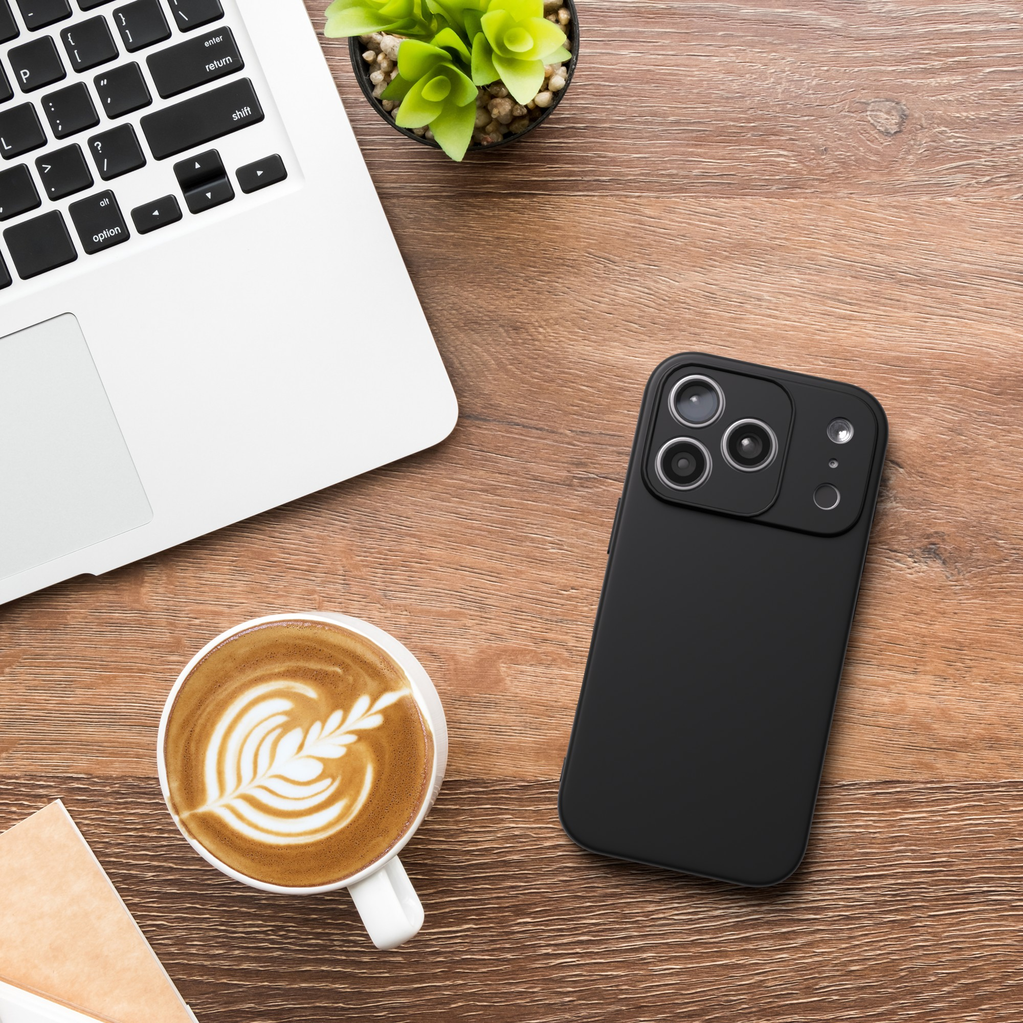 Ein Laptop, eine Kaffeetasse mit Latte Art, ein schwarzes Telefon und eine kleine Pflanze auf einem Holzschreibtisch.