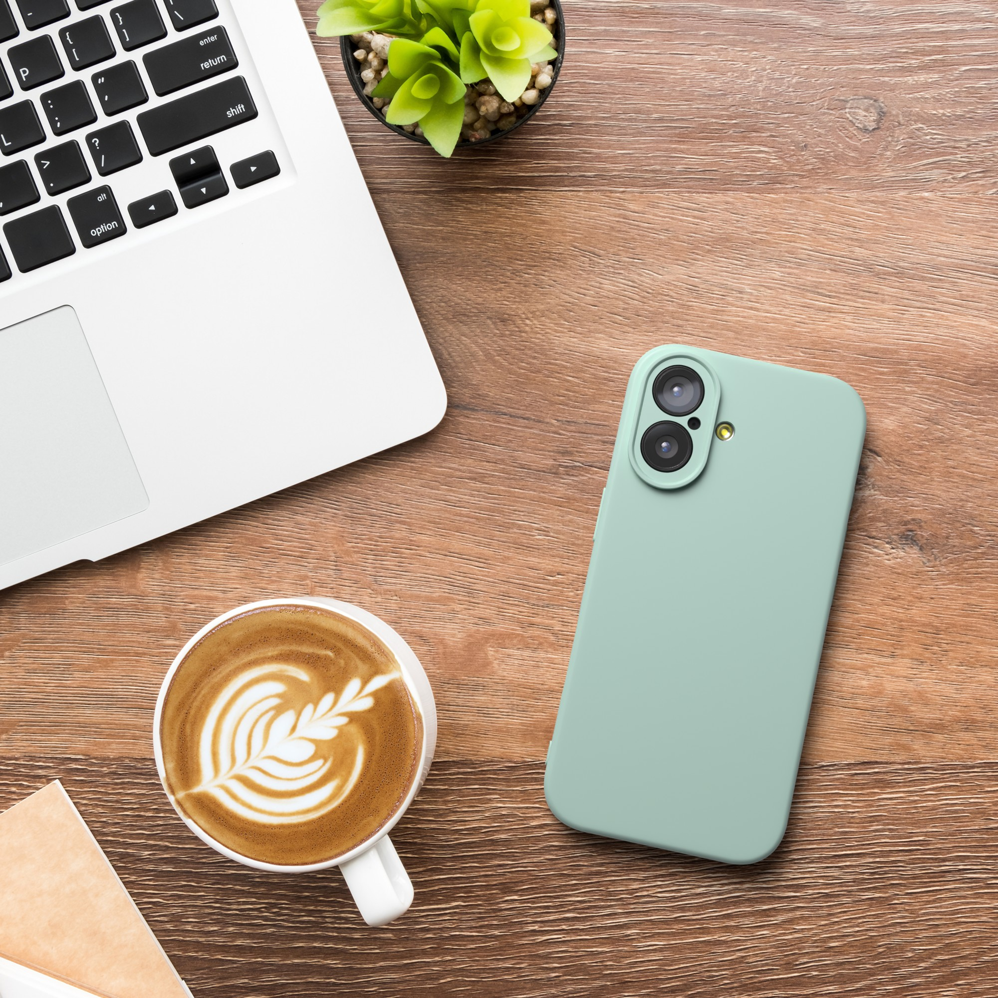 Ein Laptop, ein Telefon und eine Kaffeetasse auf einem Holztisch. Der Kaffee hat Latte Art. Es gibt eine kleine Pflanze.