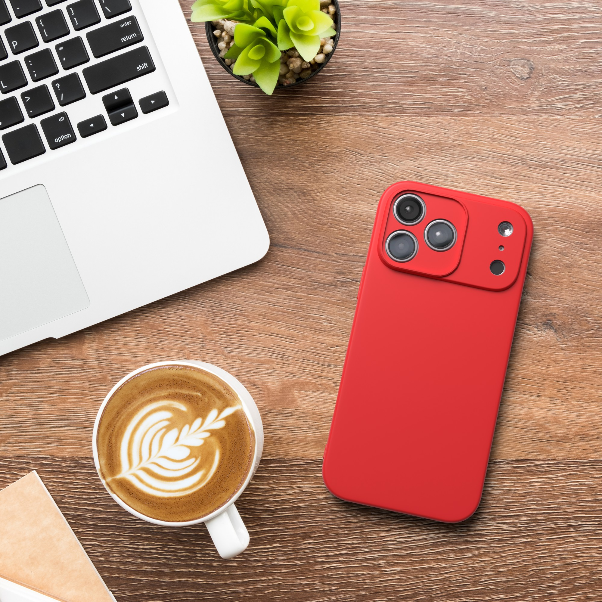 Ein rotes Telefon, Kaffee, Laptop und Pflanze stehen auf einem Holztisch. Kaffee hat ein Blattdesign.