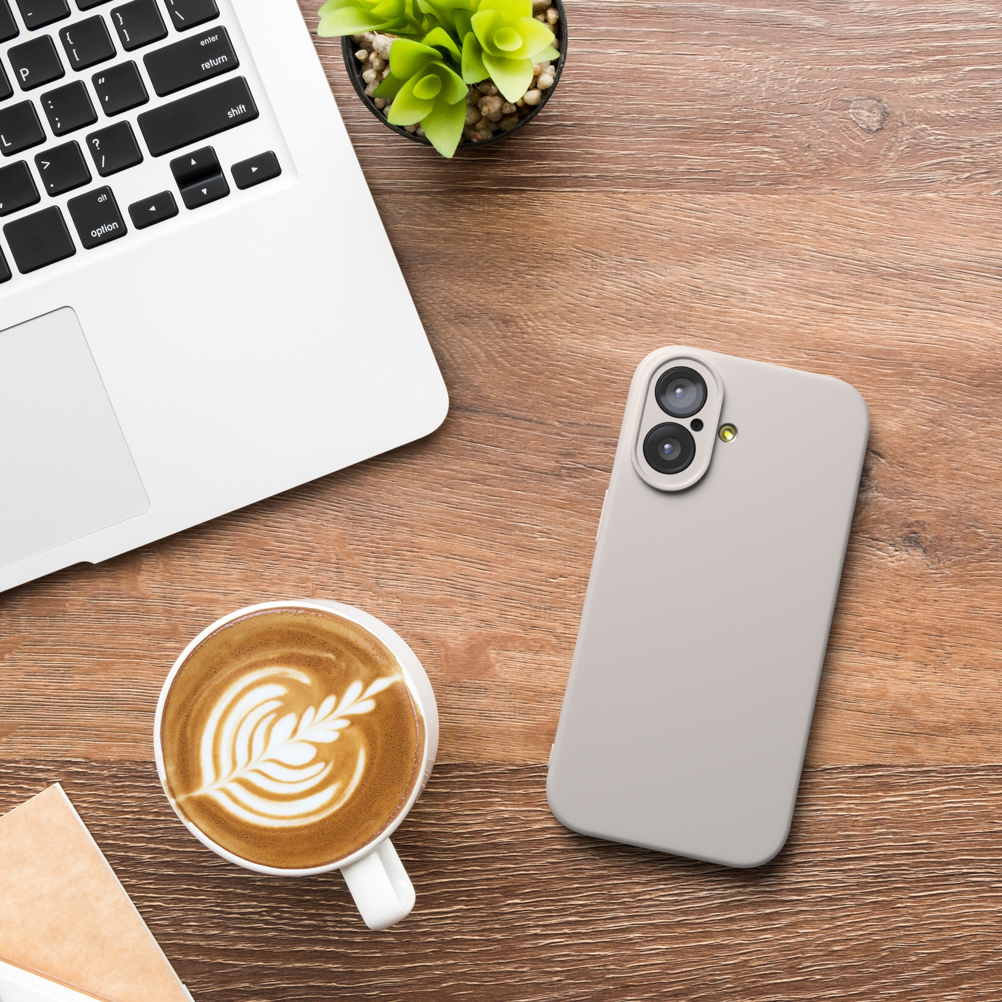 Ein Laptop, eine Kaffeetasse, ein Telefon und eine Pflanze stehen auf einem Holzschreibtisch. Kaffee hat Latte Art. Das Telefon ist hellgrau.