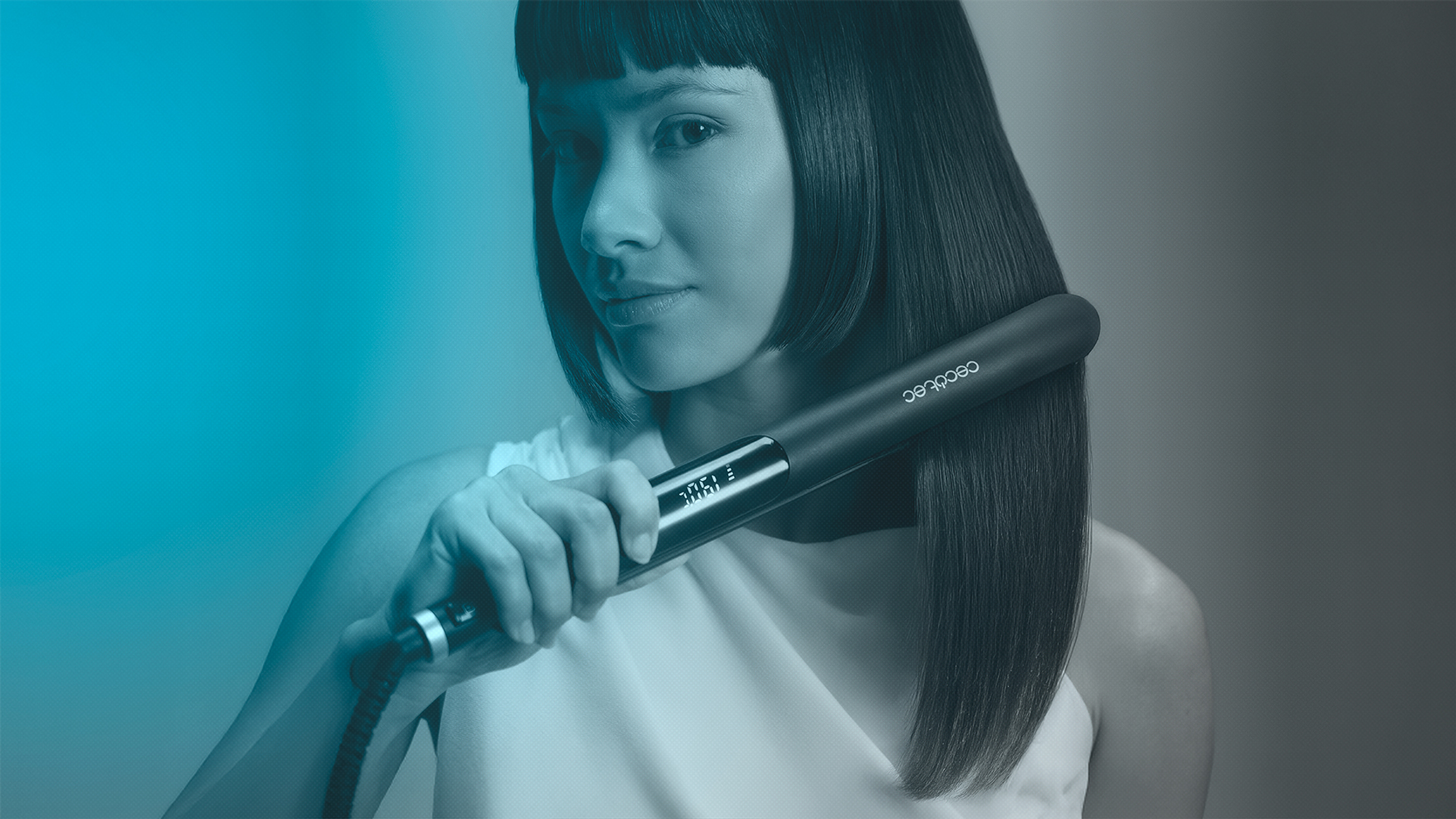Una donna usa una piastra nera sui suoi capelli scuri e lisci. Indossa un top bianco, con uno sfondo blu e grigio.