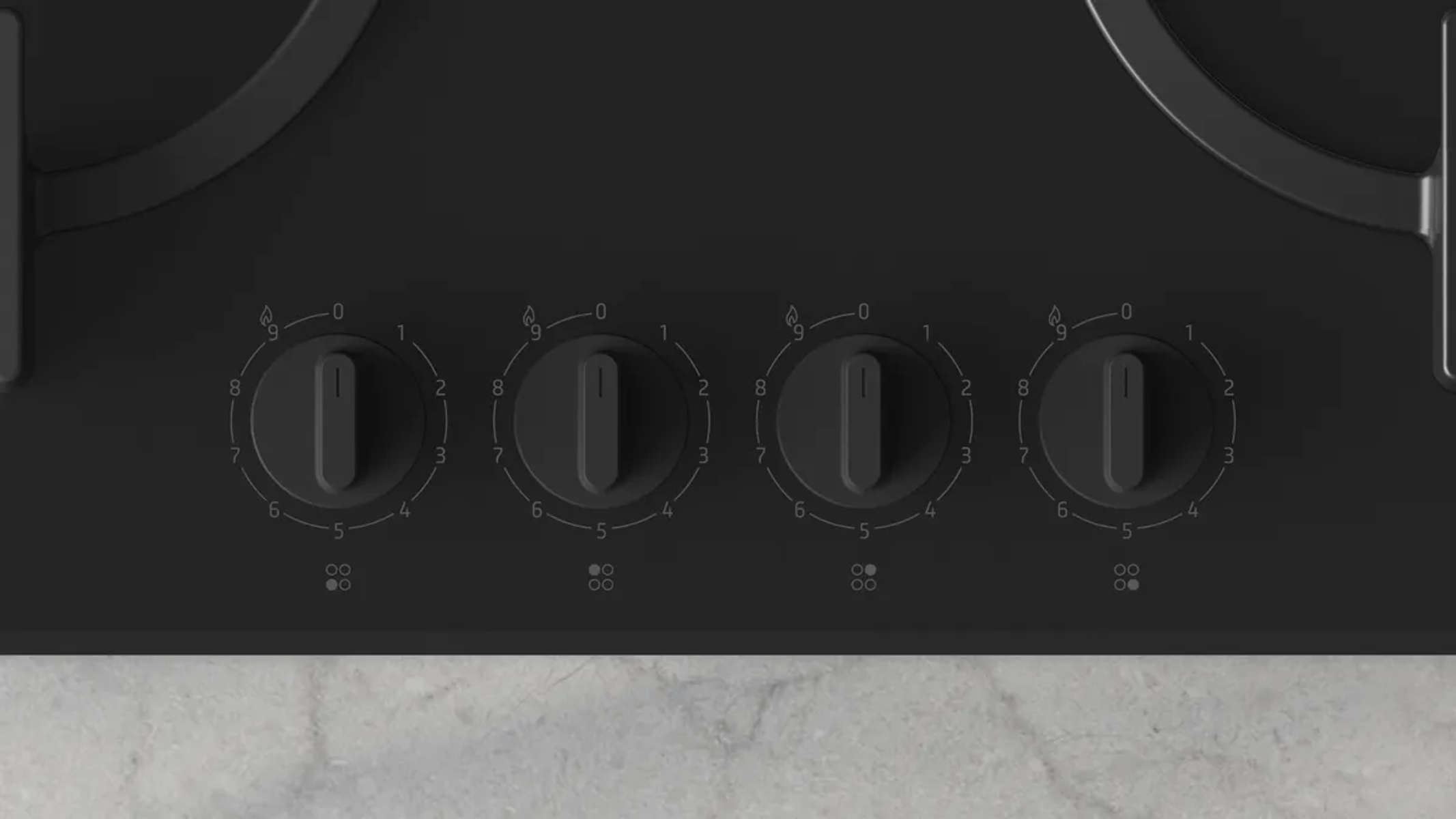 Primo piano di un piano cottura nero con quattro manopole di controllo numerate da 0 a 9. Manopole al centro, con piano di lavoro grigio chiaro.
