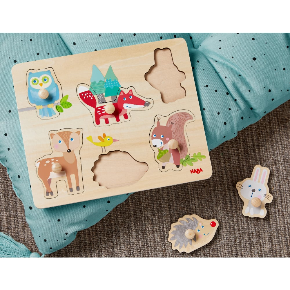 Puzzle in legno con animali della foresta. Include un gufo, una volpe, uno scoiattolo, un cervo, un uccello e un riccio. Su un cuscino blu.