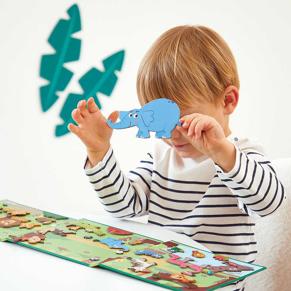 Un bambino tiene in mano un pezzo di puzzle a forma di elefante blu. Il bambino indossa una maglietta a righe. C'è un puzzle sul tavolo.