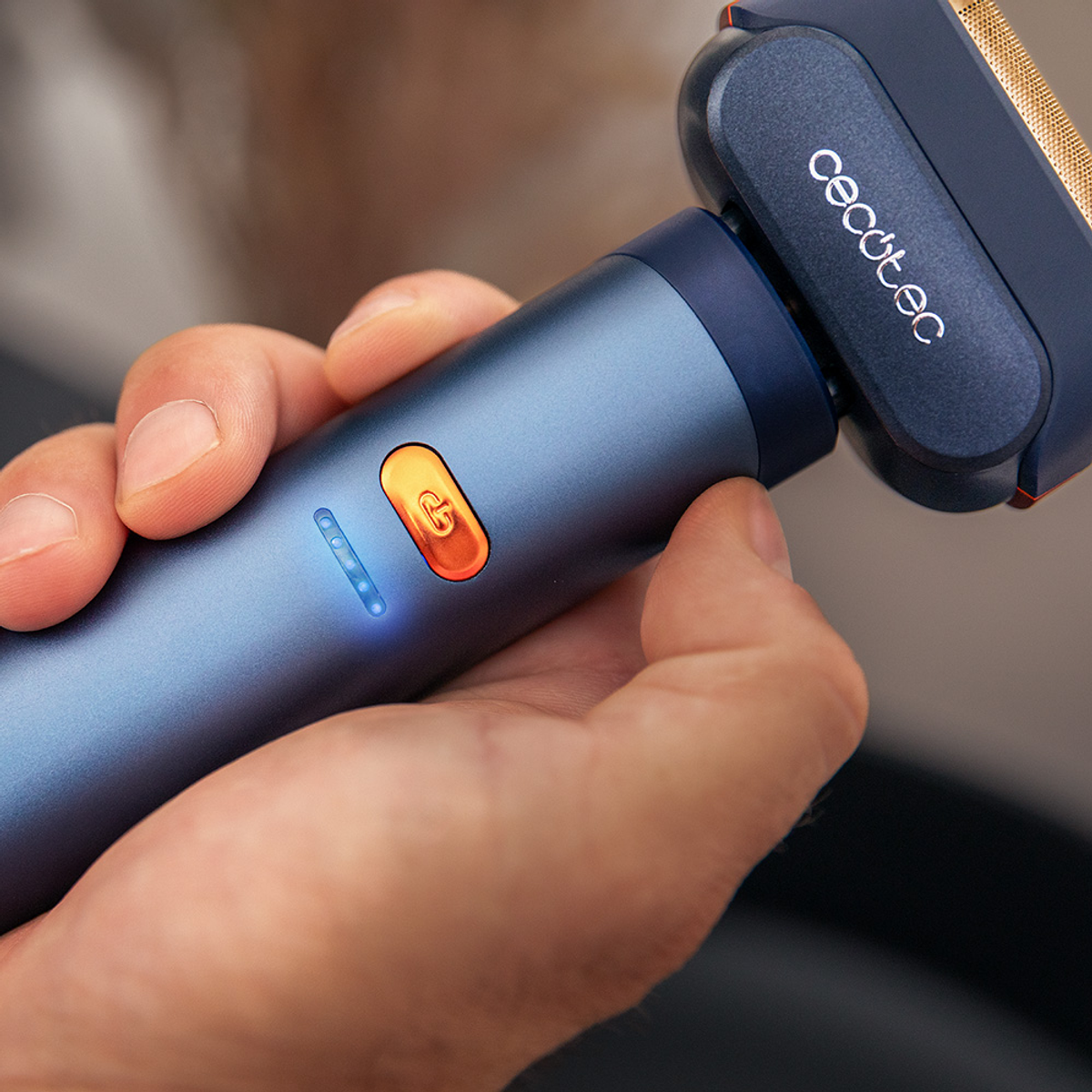 Una mano tiene un rasoio elettrico blu e arancione. Il rasoio ha il marchio 'cecotec' sulla testina.