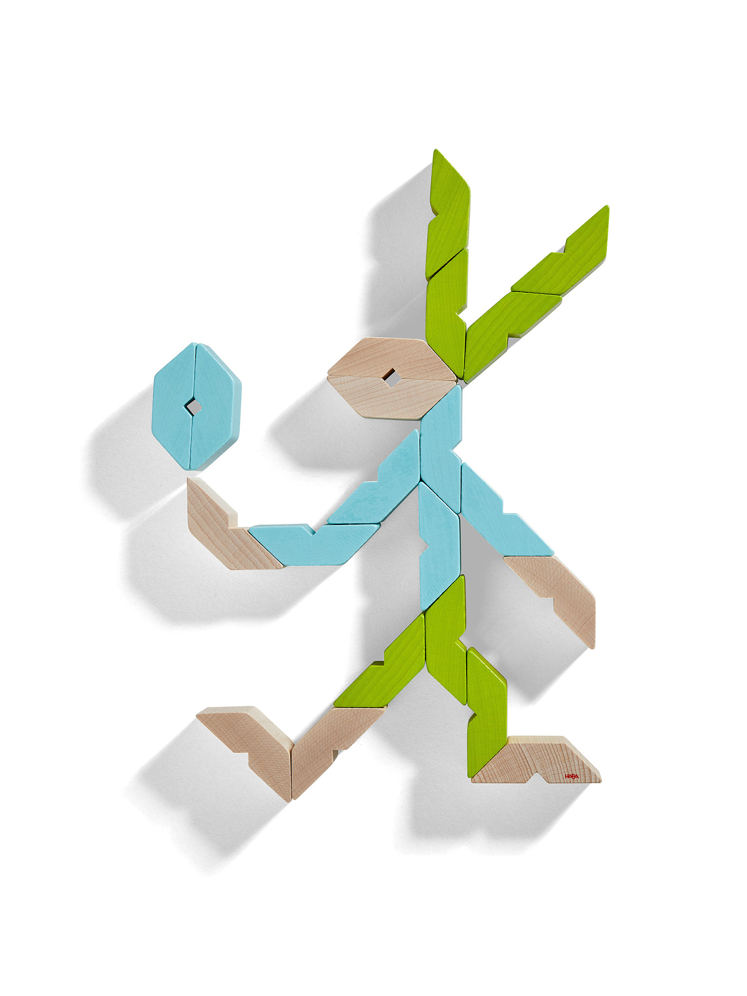 Postać wykonana z drewnianych klocków w kolorze niebieskim, zielonym i beżowym na białym tle. Przypomina ludzika.