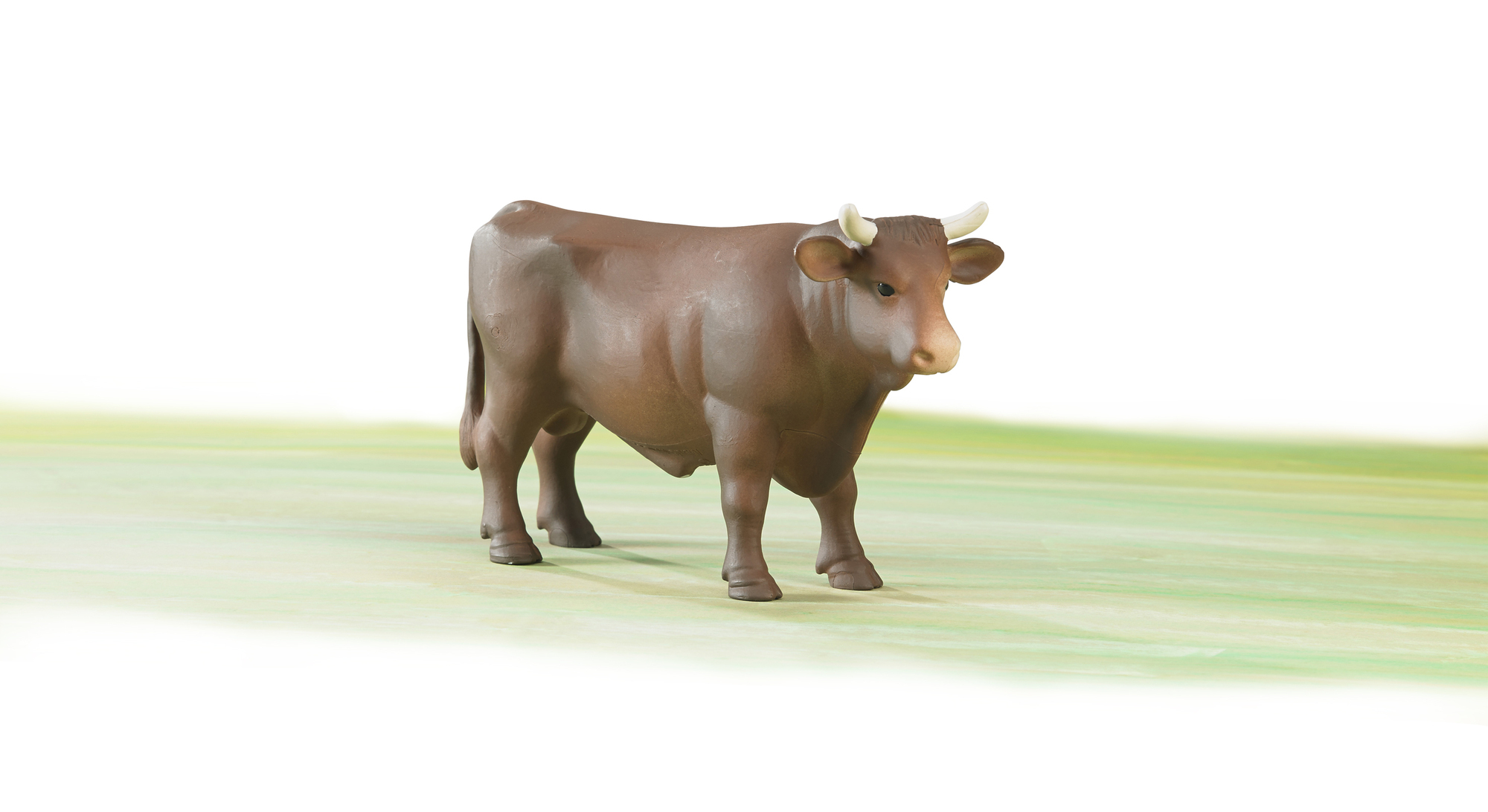 Eine braune Bullenfigur steht auf einer hellgrünen Oberfläche mit weißem Hintergrund. Der Bulle hat weiße Hörner und eine beige Schnauze.