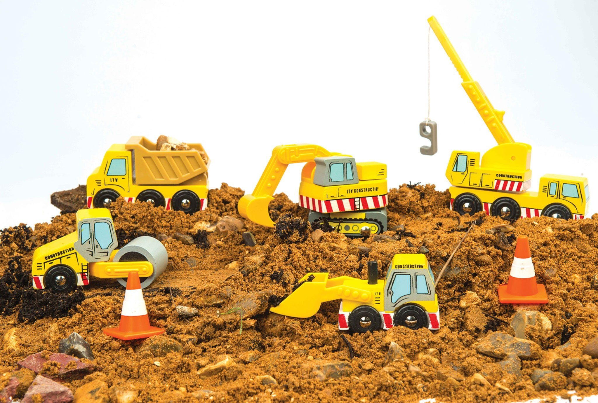 Vehículos de construcción de juguete sobre tierra: volquete, excavadora, rodillo, grúa y excavadora. También hay dos conos de tráfico.