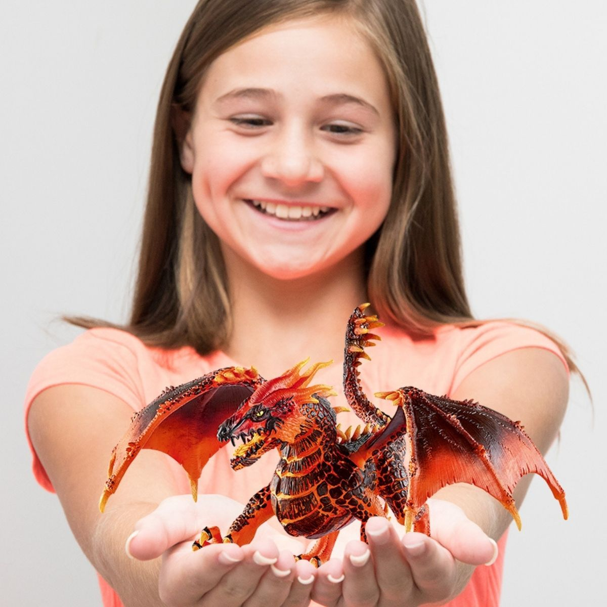 Dziewczyna uśmiecha się, trzymając szczegółowego smoka. Smok jest czerwony, pomarańczowy i czarny. Tło jest białe.