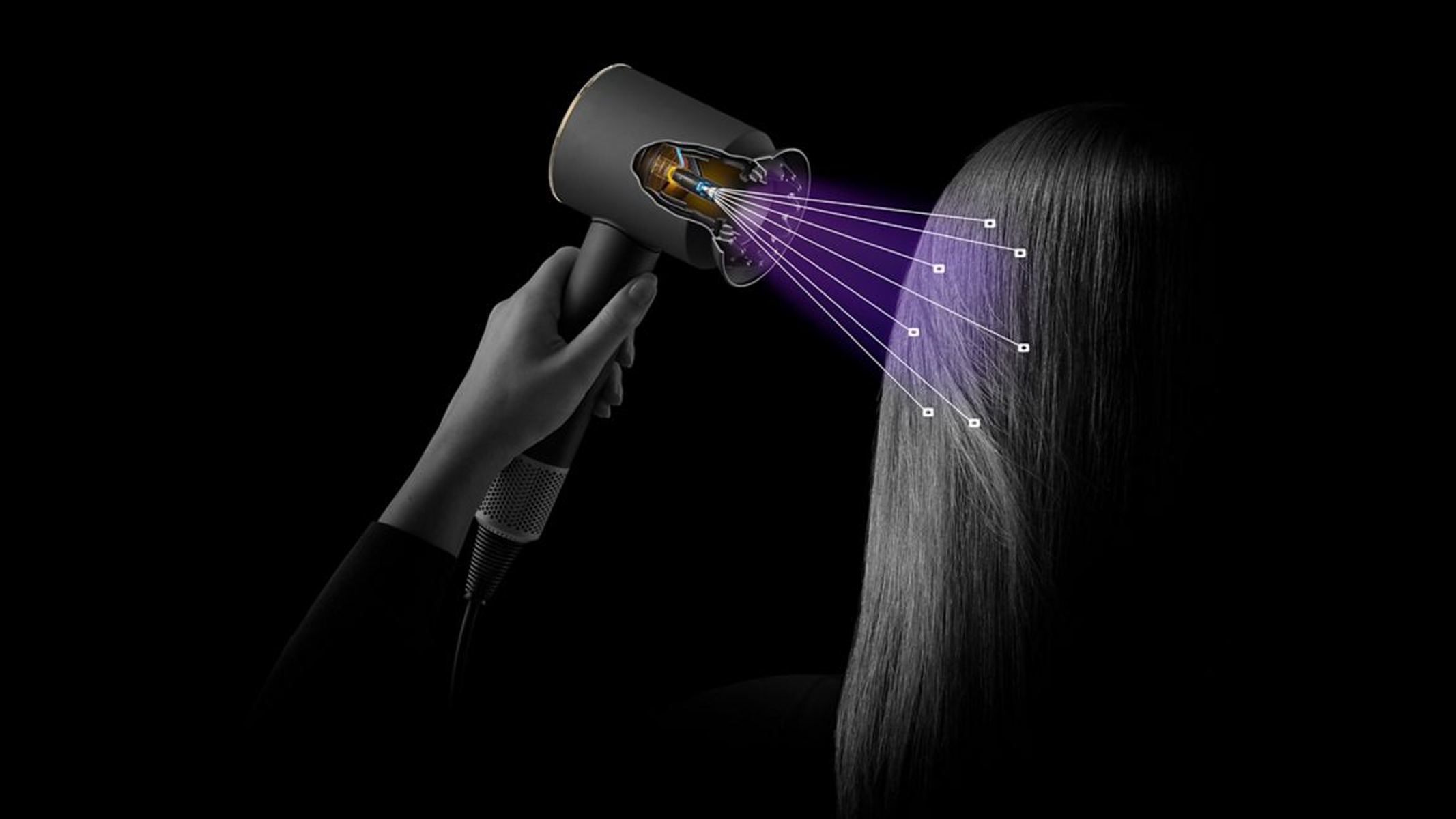 Eine Person benutzt einen schwarz-grauen Föhn für ihr Haar. Lila Luft strömt aus dem Föhn auf das Haar. Schwarzer Hintergrund.
