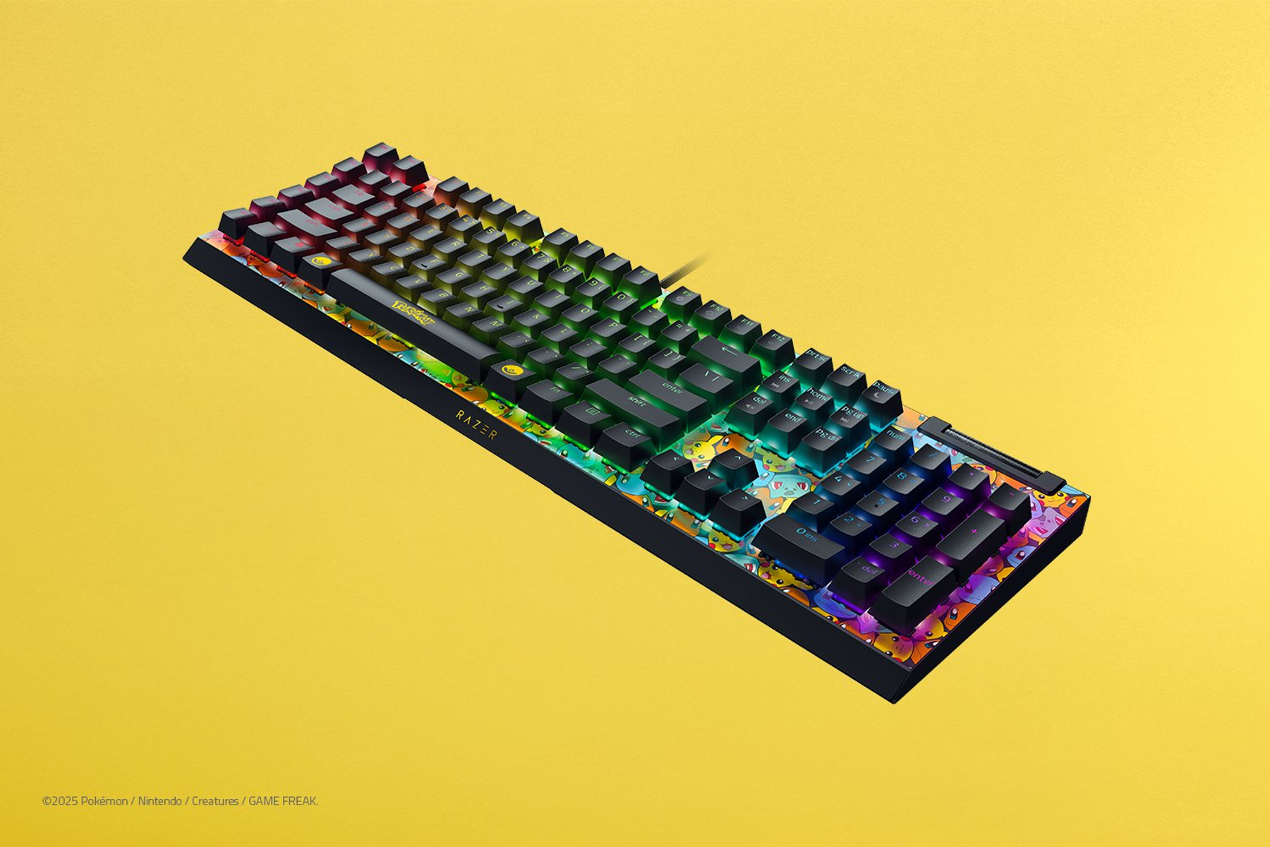 Klawiatura Razer z czarnymi klawiszami i podświetleniem RGB. Ma motyw Pokémon, z postaciami na dolnej krawędzi, na żółtym tle.