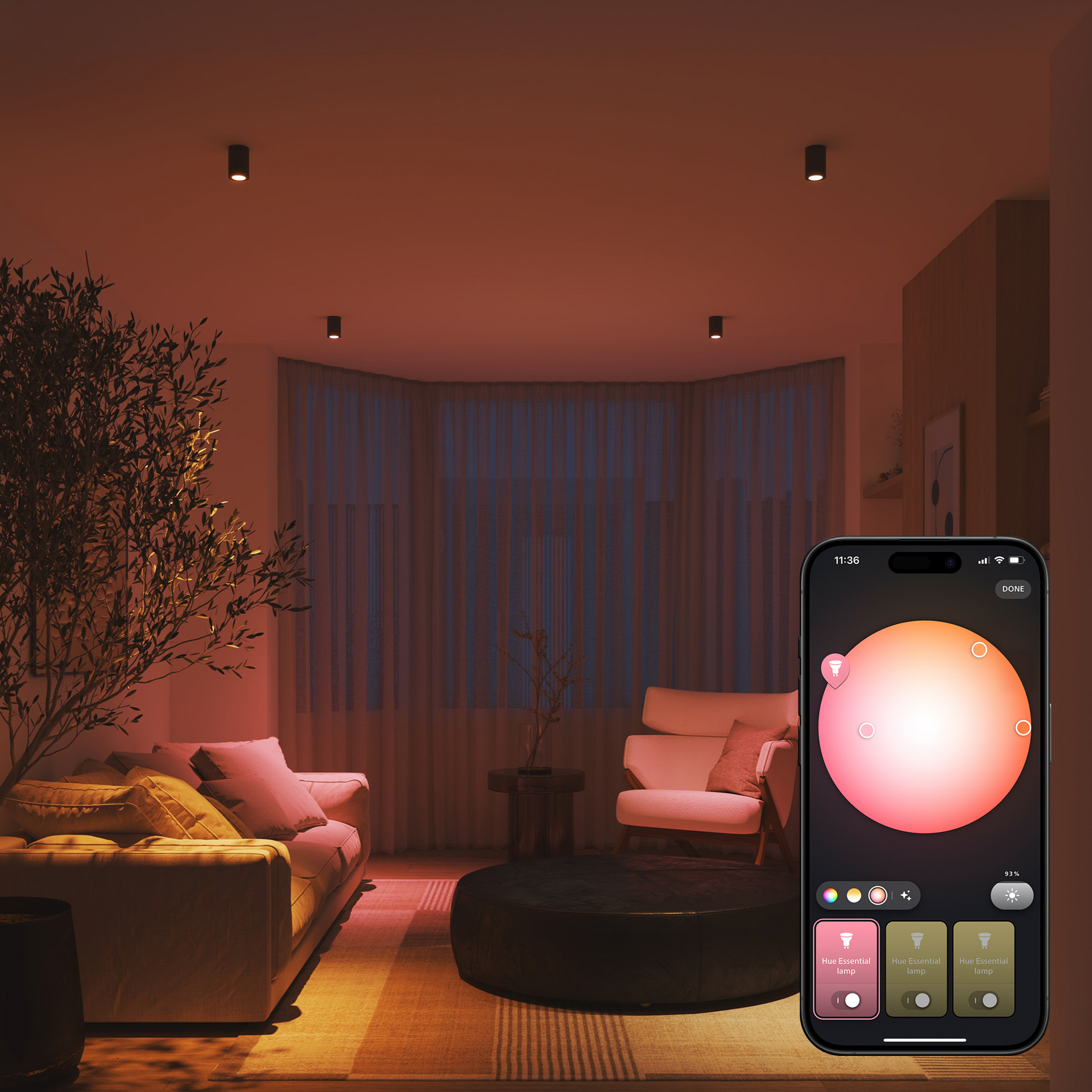 Wohnzimmer mit rotem Licht beleuchtet. Ein Telefon zeigt Lichtsteuerungen. Sofa, Sessel und Baum im Raum. Deckenleuchten sind sichtbar.