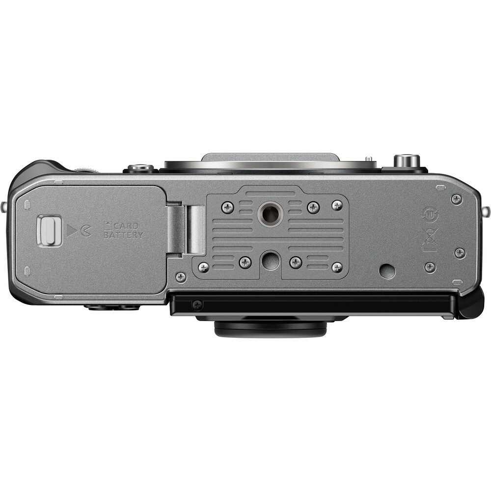 Bovenaanzicht van een zilveren camera, met batterij- en kaartsleuven, samen met diverse knoppen en schroefdetails, tegen een witte achtergrond.