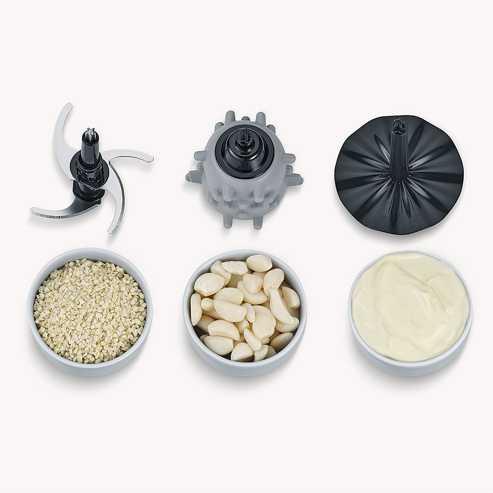 Un robot da cucina smontato con lame, una parte del motore, un coperchio e tre ciotole con aglio tritato, aglio intero e salsa.