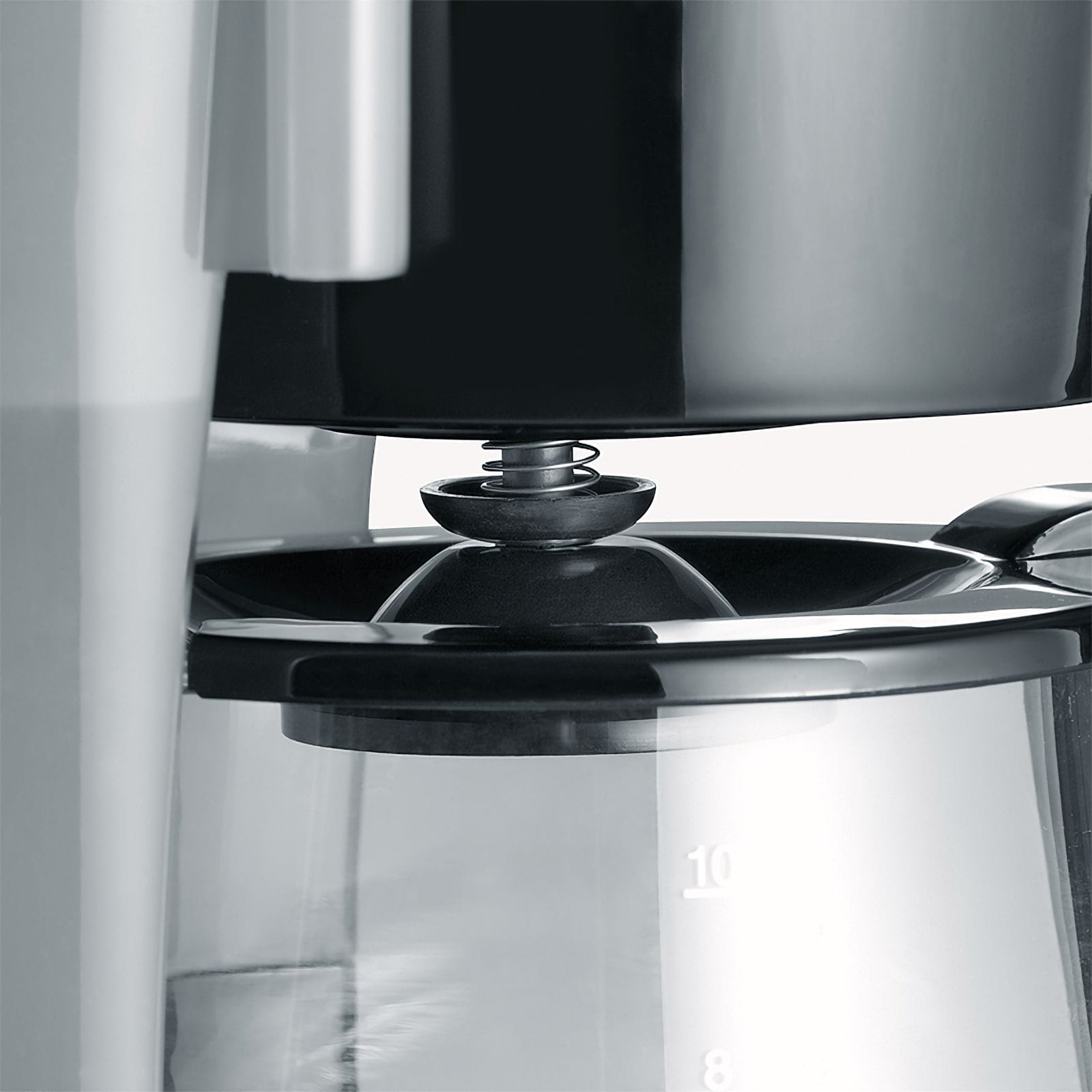 Zbliżenie ekspresu do kawy. Widoczna czarna pokrywa, sprężyna, szklana karafka z oznaczeniami i biała plastikowa część.