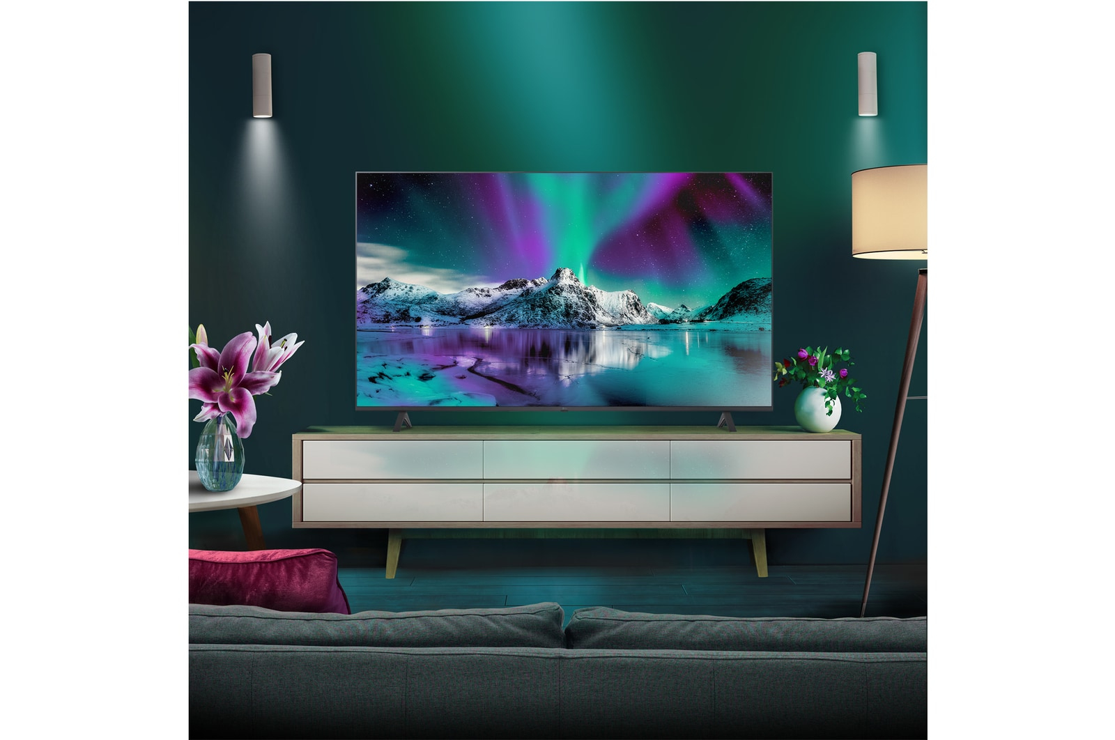Salón con TV mostrando aurora boreal. Flores, lámpara y un mueble moderno en la habitación.