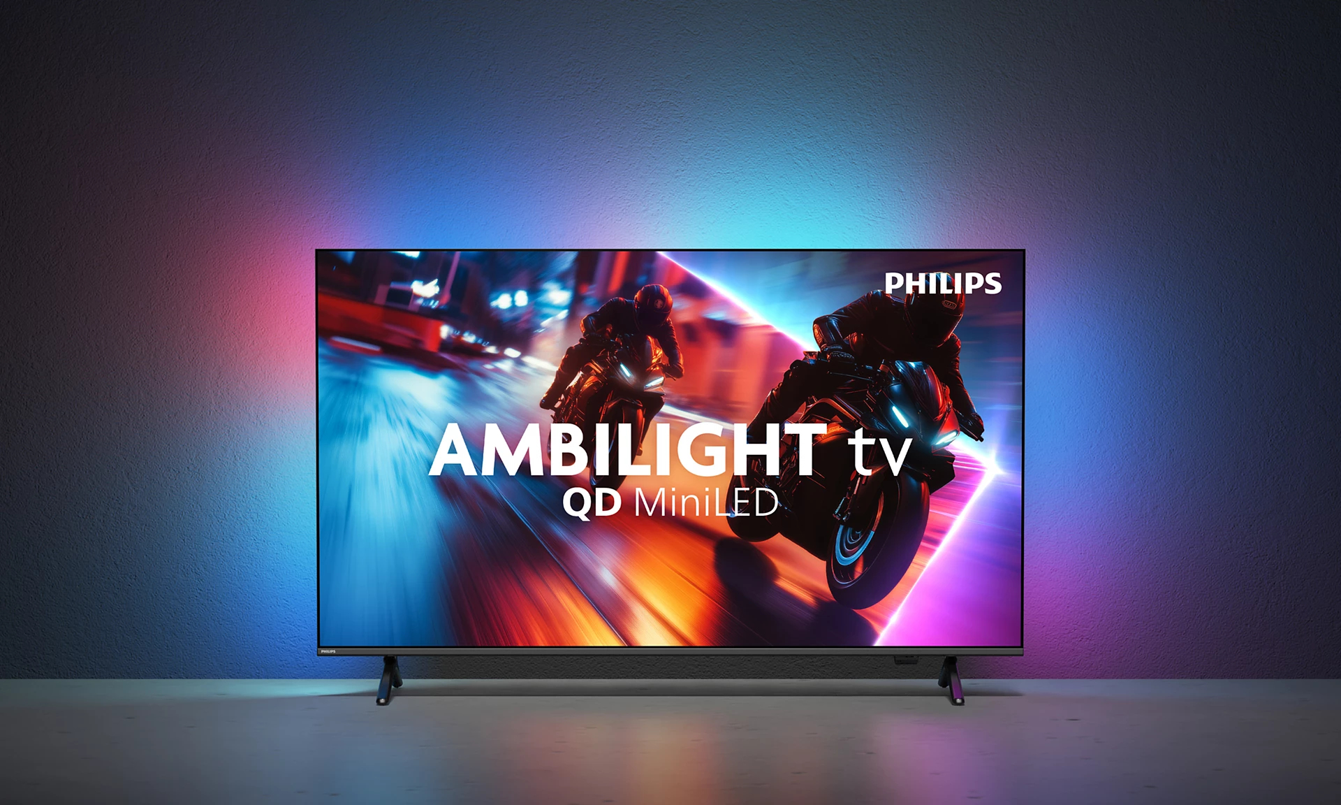 Telewizor Philips Ambilight wyświetla dwóch motocyklistów w wyścigu. Tło to gradient niebieskiego, różowego i fioletowego na teksturowanej ścianie.