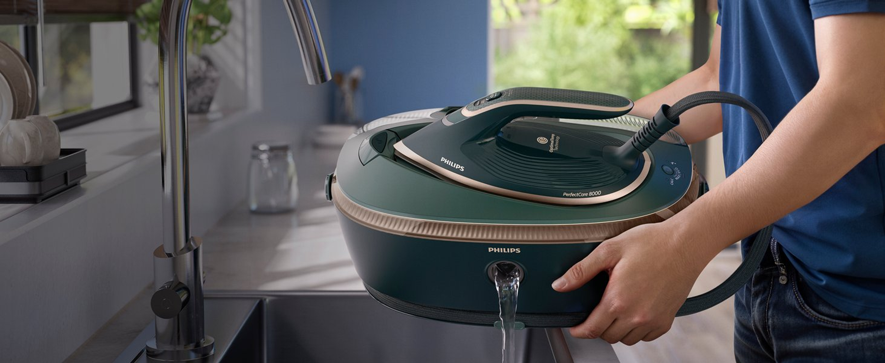 Una persona sostiene una plancha Philips PerfectCare 8000 verde y dorada, con agua saliendo. Un grifo y un fregadero están en el fondo.