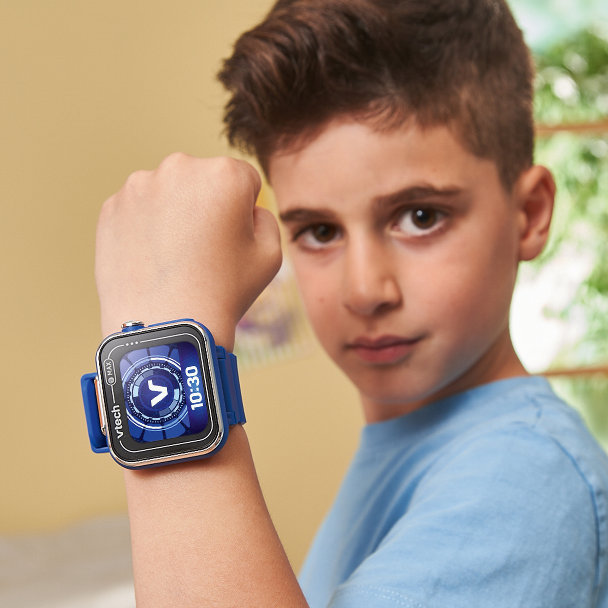 Un niño con un reloj inteligente azul, mostrando 10:30. Lleva una camisa azul. El fondo es amarillo suave con un toque de verde.