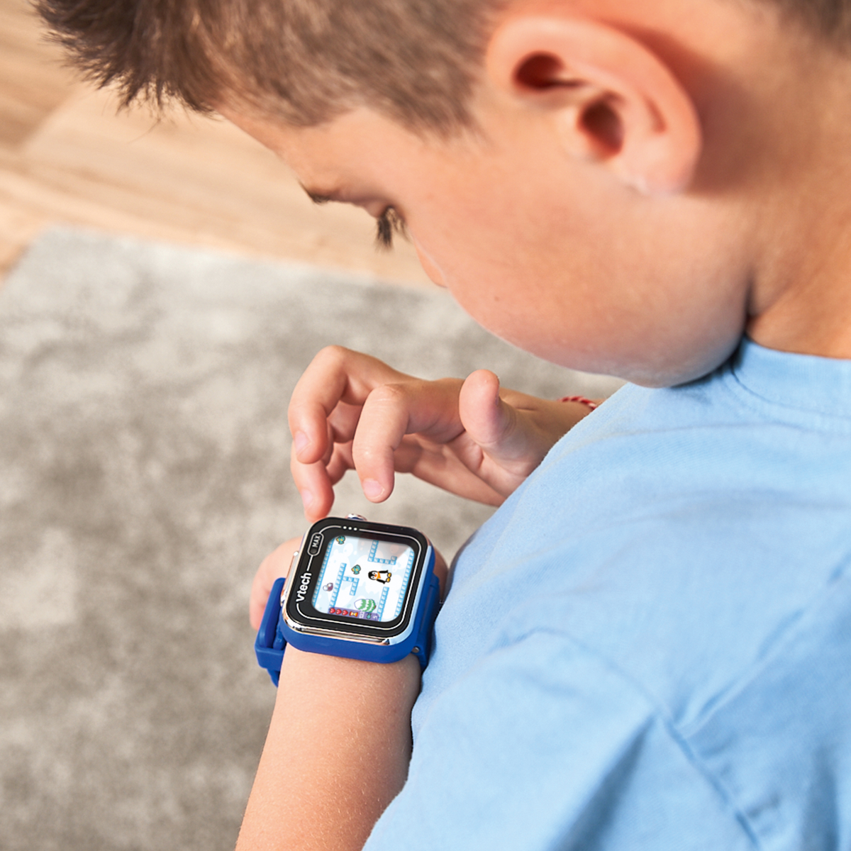 Un niño mira un reloj inteligente que muestra un juego. El reloj es azul y negro. El niño lleva una camisa azul.