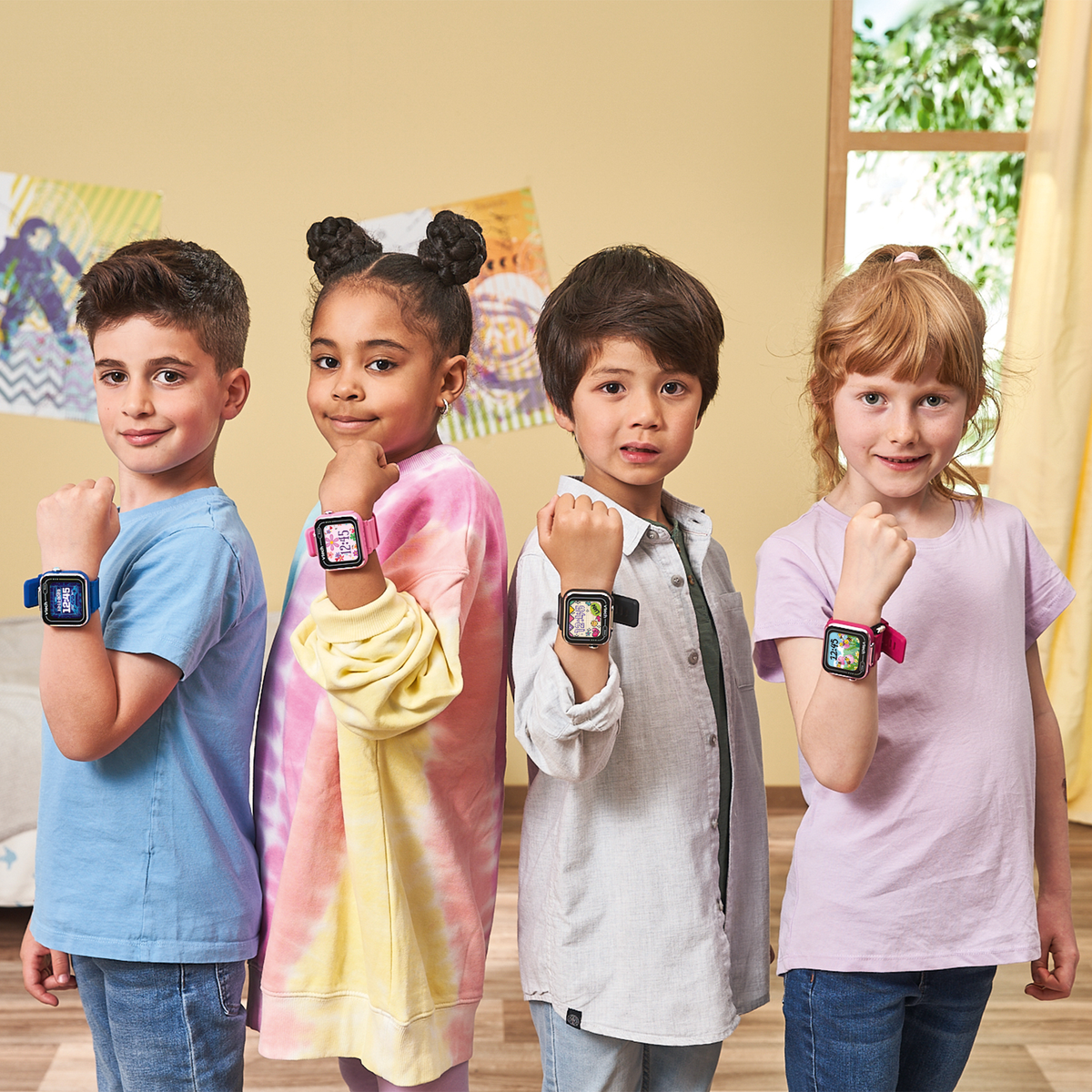 Cuatro niños posan con smartwatches. Están frente a una pared amarilla. Se ven relojes y ropa coloridos.
