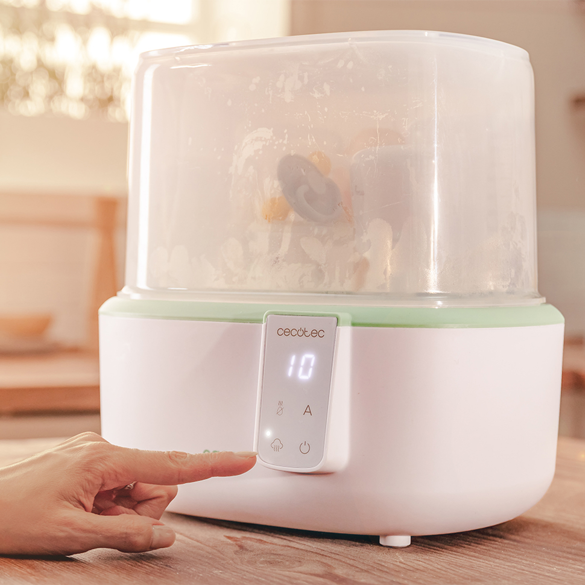 Ein weiß-grüner Babyflaschensterilisator. Eine Hand drückt eine Taste auf der Frontplatte. Das Display zeigt die Zahl 10.