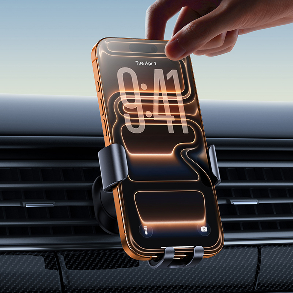 Una mano inserisce uno smartphone in un supporto per bocchetta dell'auto. Il telefono mostra le 9:41, contro cruscotto e cielo blu.