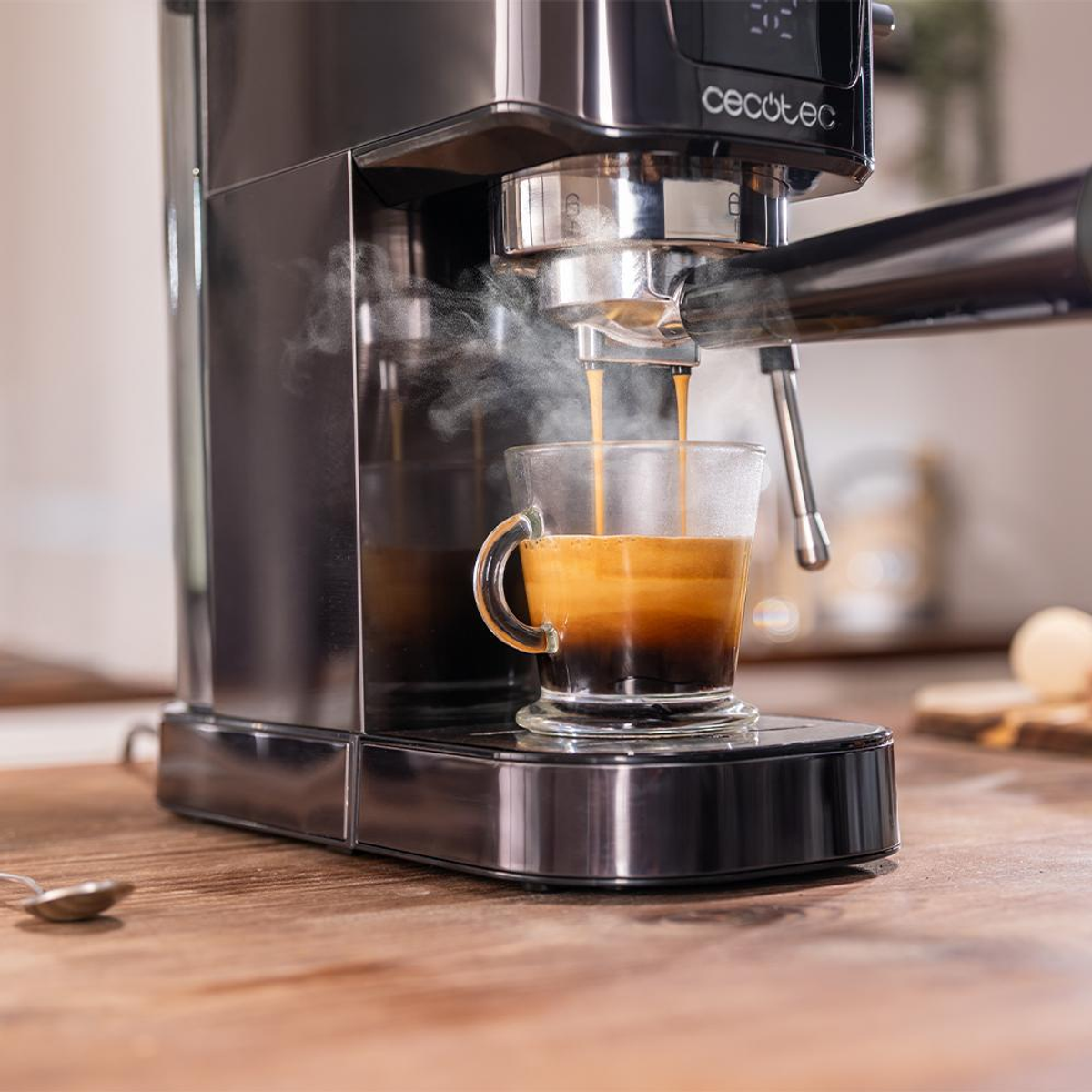 Macchina per espresso che prepara il caffè in una tazza di vetro. Il vapore sale. Cucchiaio e tagliere sullo sfondo sfocato.