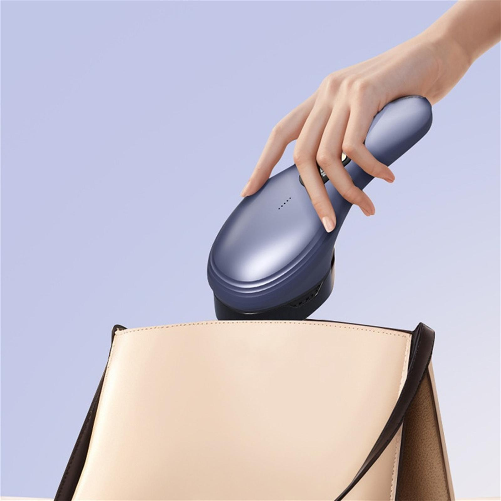 Eine Hand legt ein blaues Gerät in eine beige Handtasche. Der Hintergrund ist ein Blauton.
